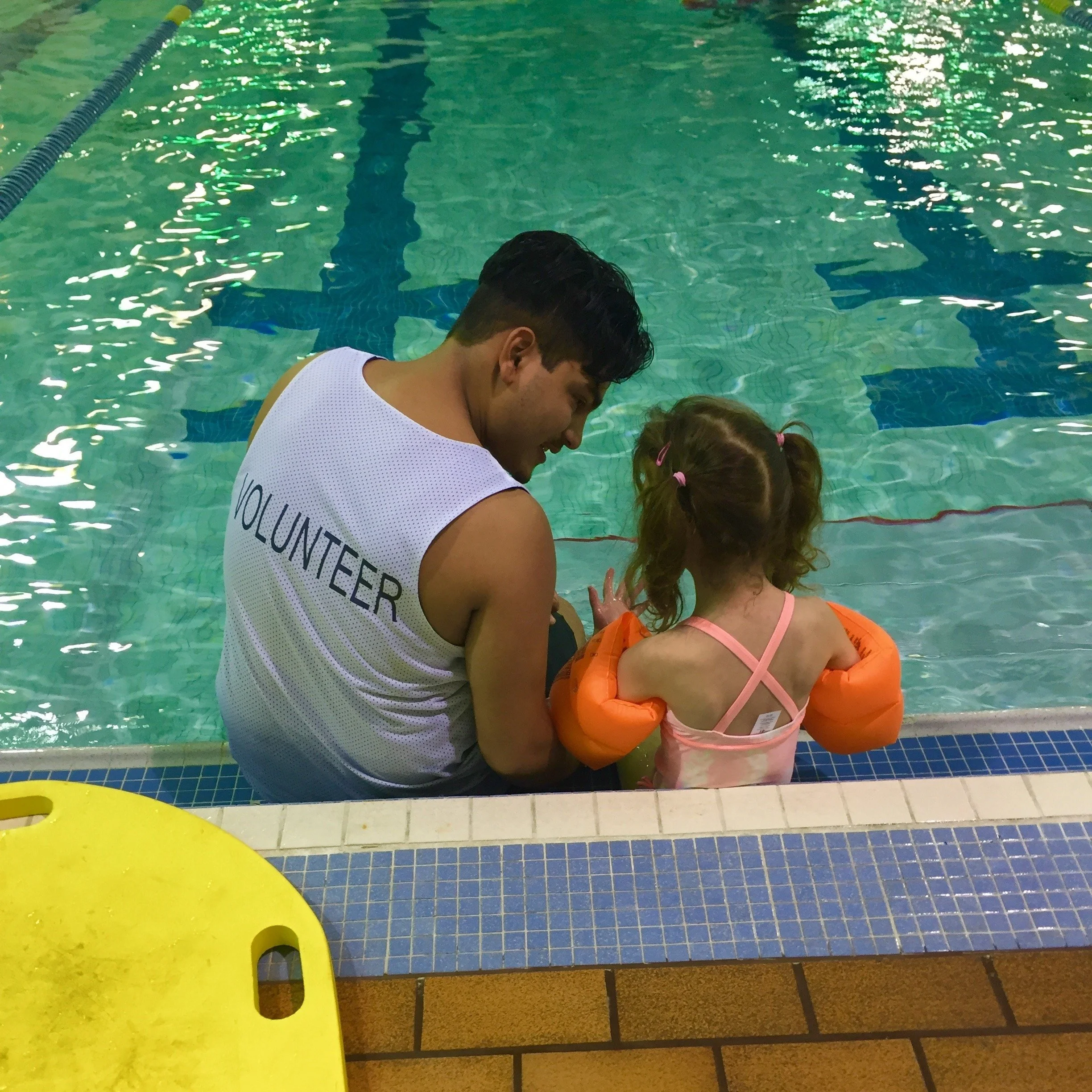 SWAM swimmer-instructor pair sitting on the edge of the pool, from the back
