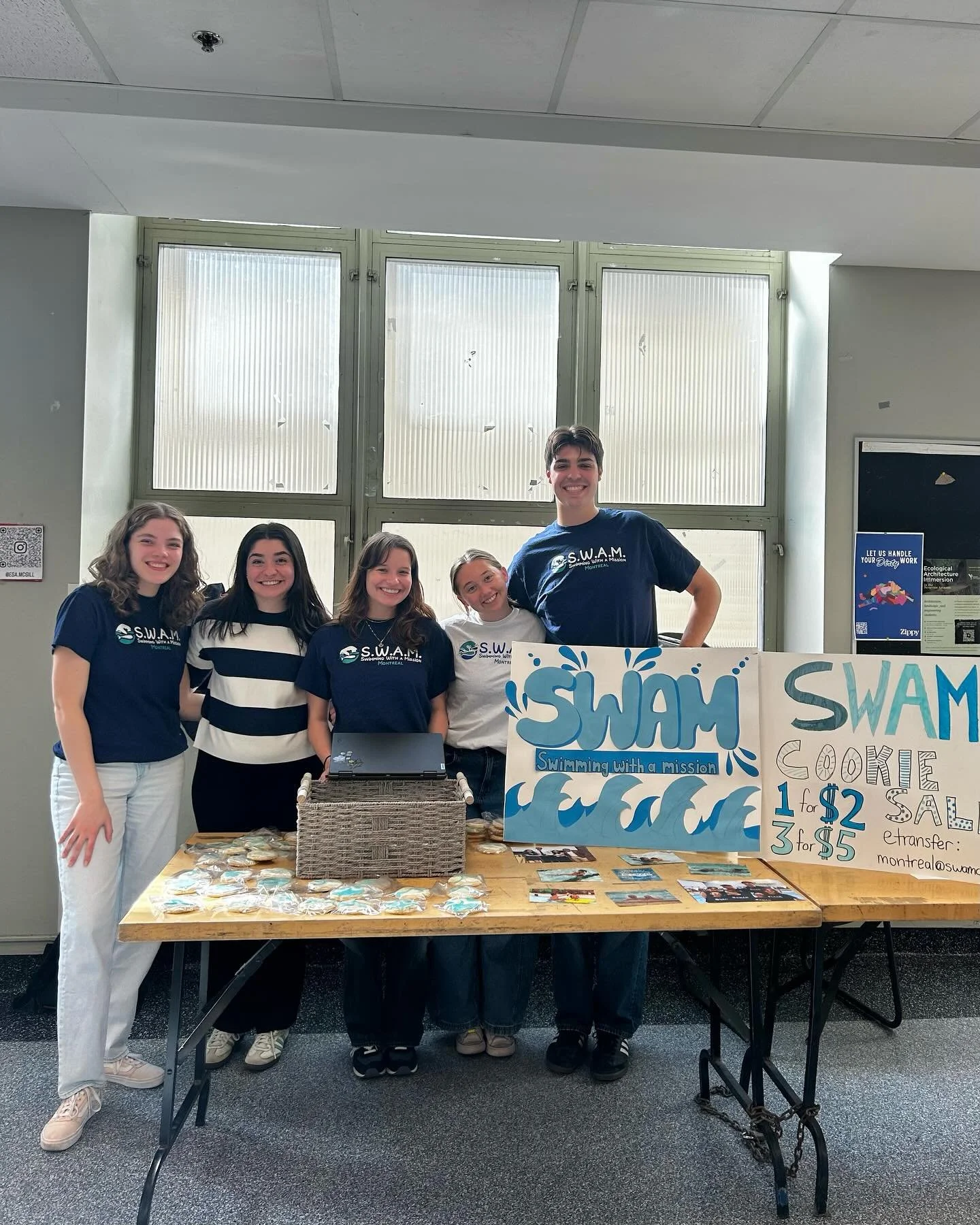five SWAM Montreal volunteers standing at a table with posters that say "SWAM"
