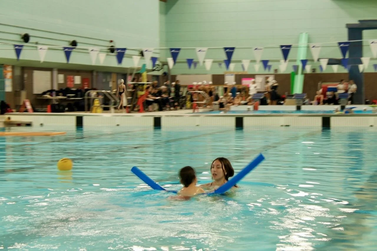 swimmer using noodle, swimming toward instructor