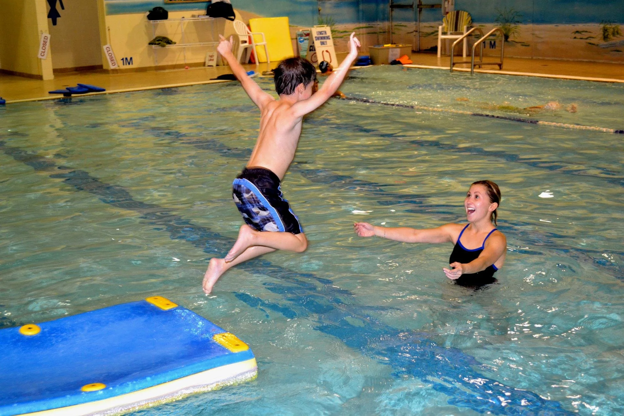 swimmer jumping off a floating mat towards smiling instructor
