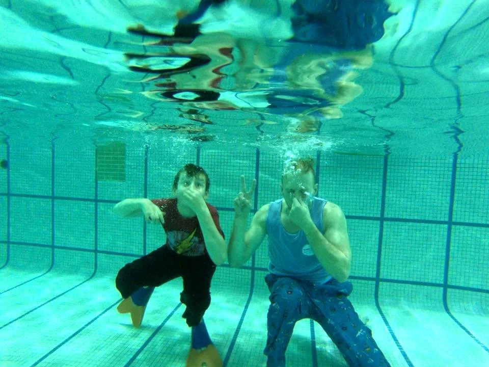 clothed swimmer and instructor plug their noses underwater