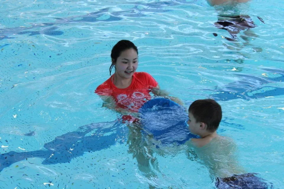 swimmer holding flutter board, kicking towards smiling instructor