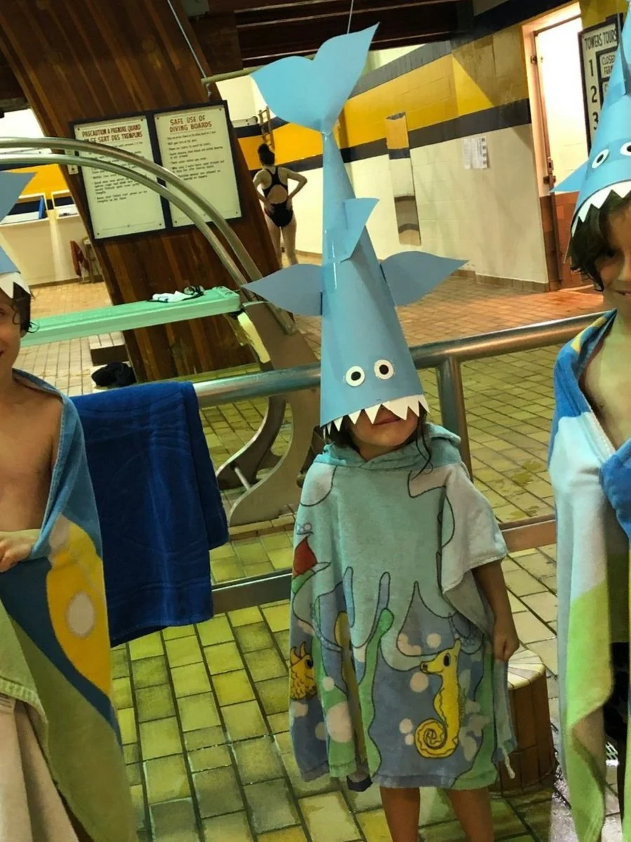 SWAM swimmer with a silly shark hat, more swimmers out of frame