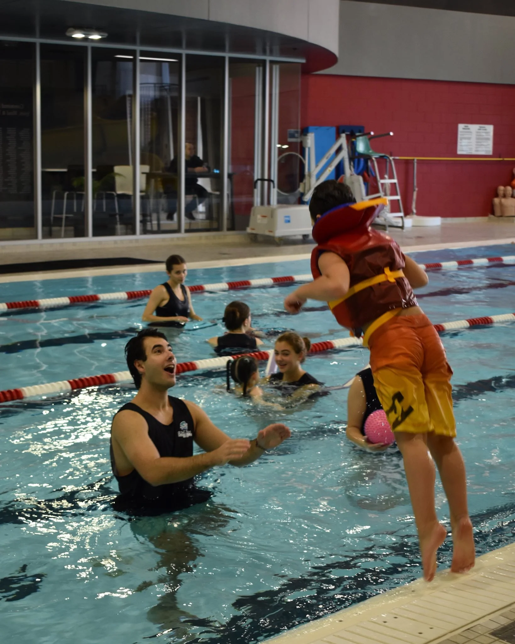 Child in red lifejacket jumping into pool