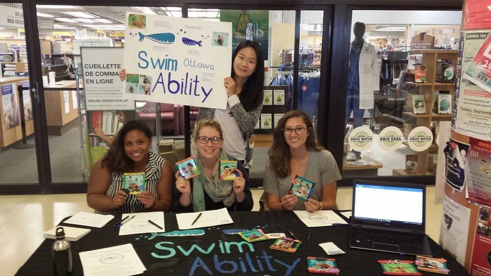 group of smiling SwimAbility Ottawa volunteers tabling at a clubs fair