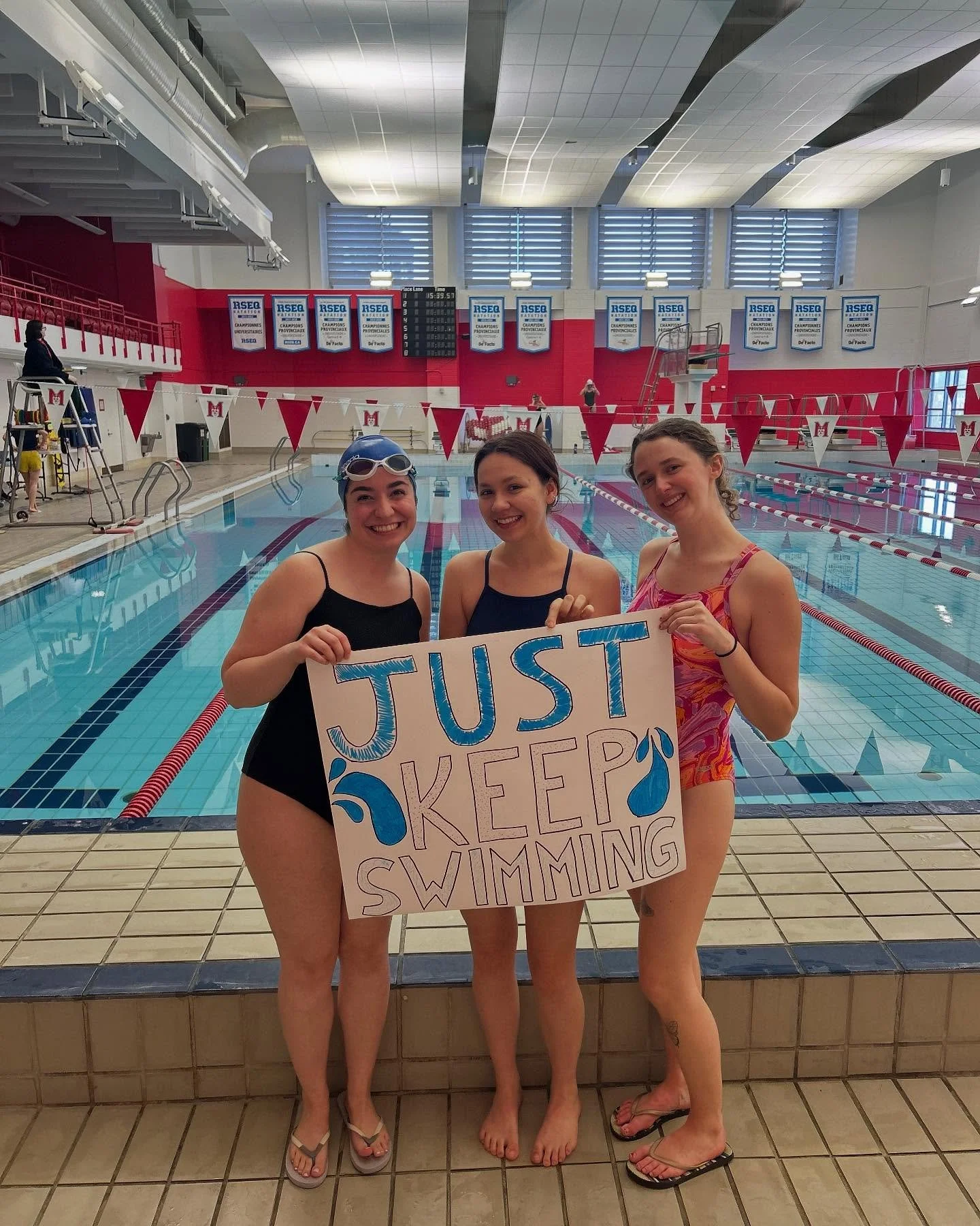 instructors smiling on the pool deck with a sign that says "just keep swimming"