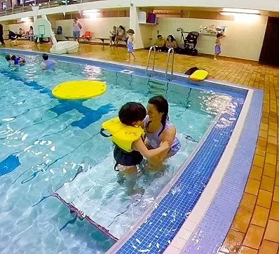 swimmer wearing lifejacket standing on tot-dock with instructor