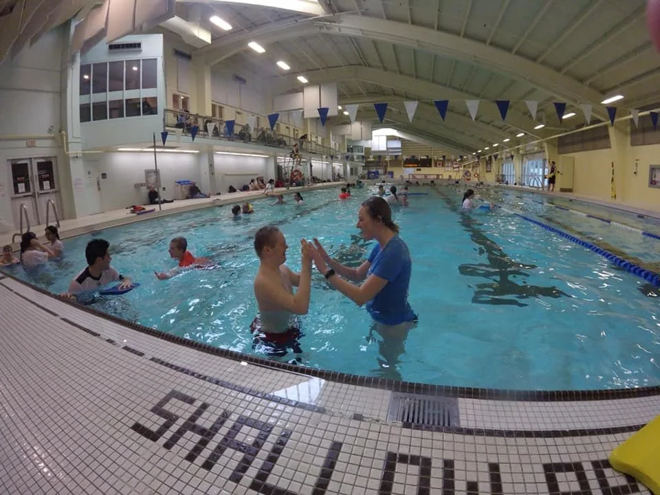 SWAM swimmer and instructor sharing a high five, with other swimmer-instructor pairs in the background