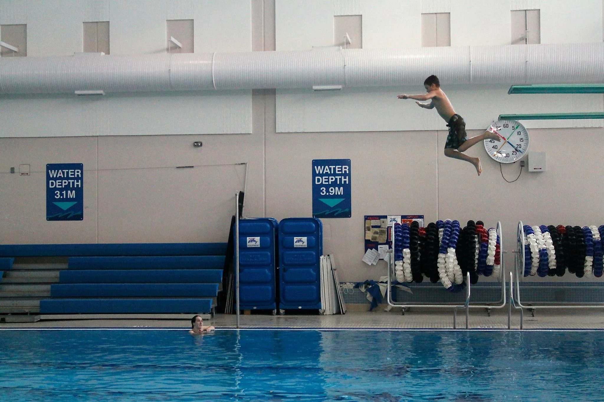 swimmer jumping off the diving board with instructor watching and smiling