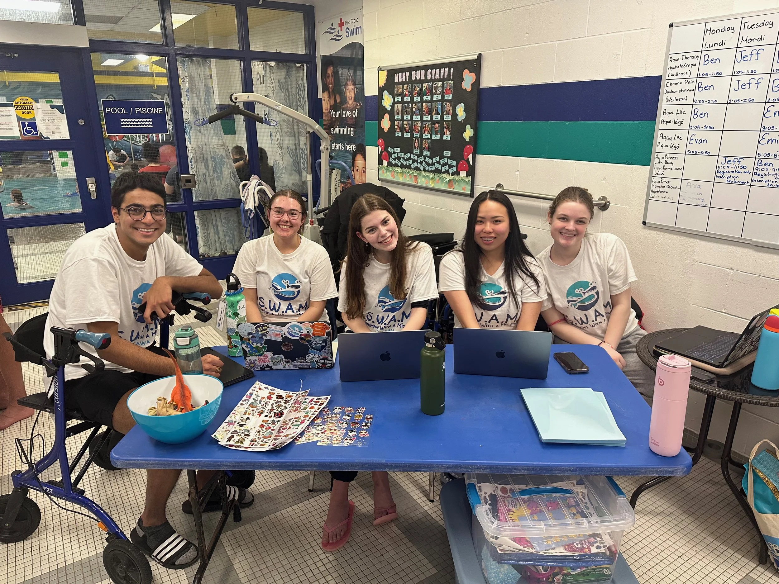 group of five SWAM Ottawa volunteers sitting at a table, wearing matching SWAM shirts