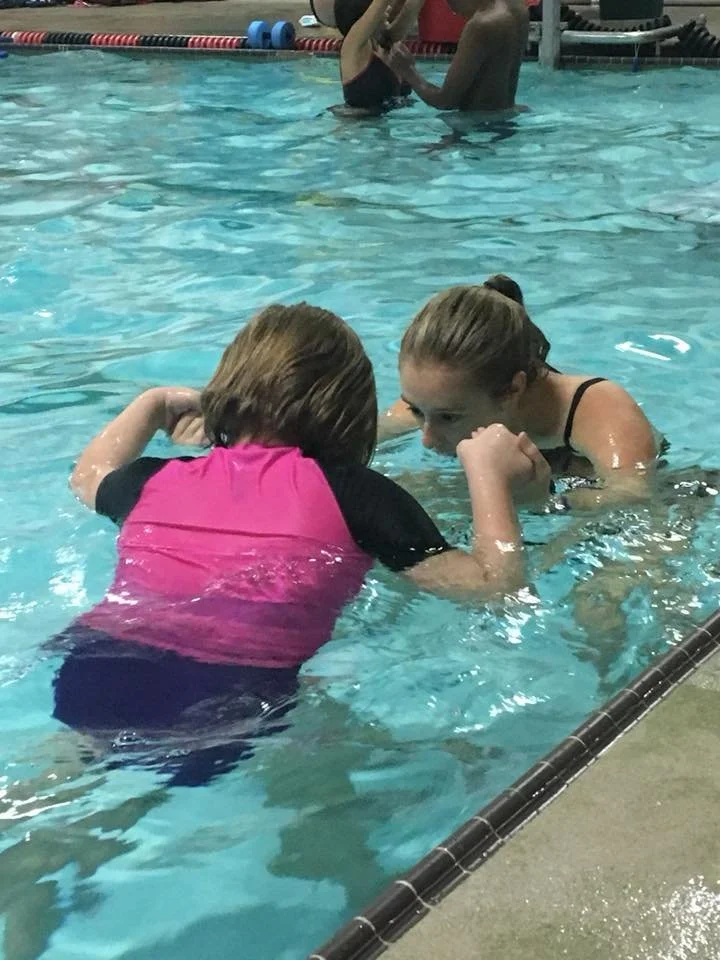 swimmer and instructor blowing bubbles together and holding hands