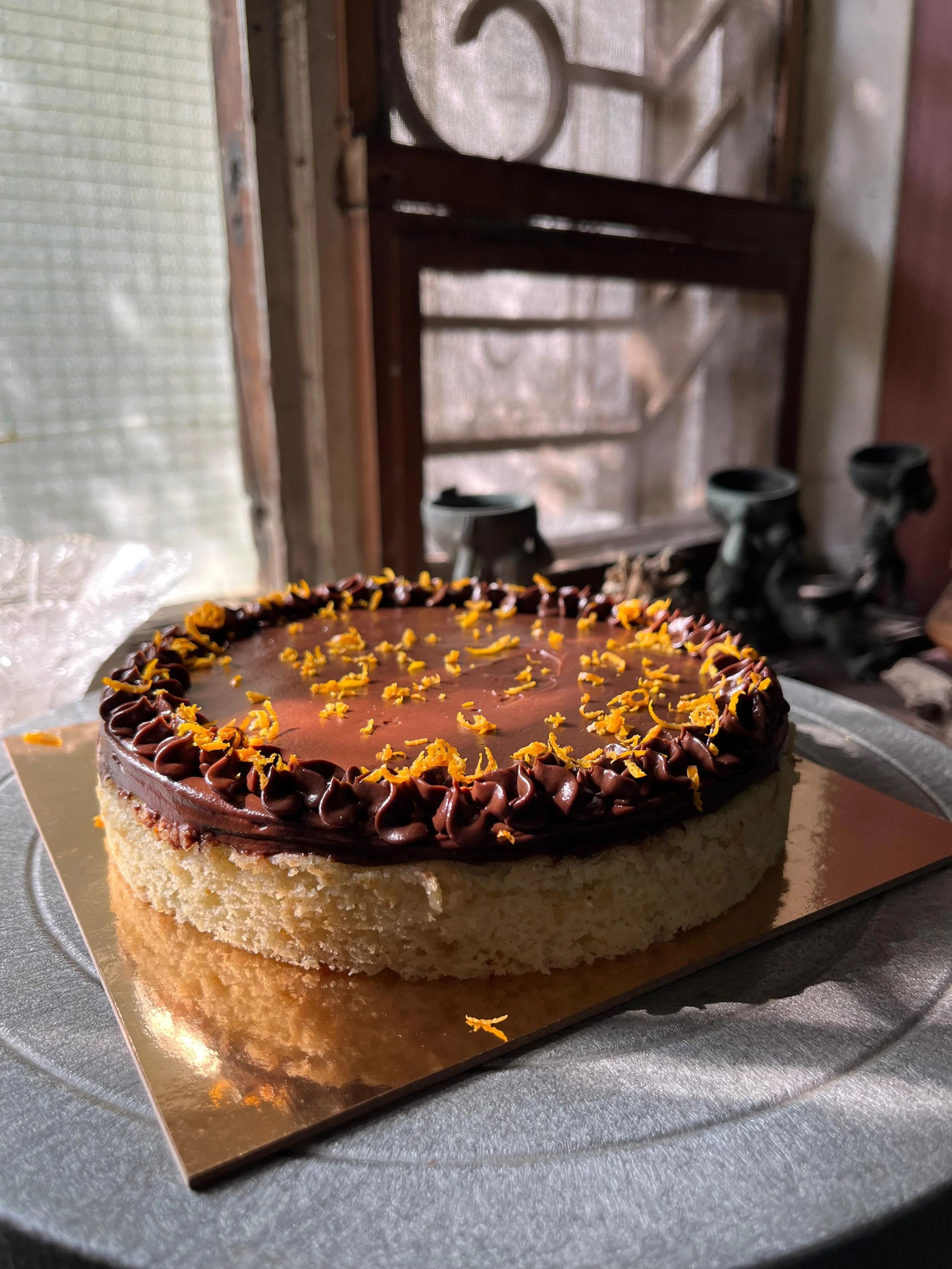 Chocolate cake with orange zest on top, on a golden board, placed on a metal platter.