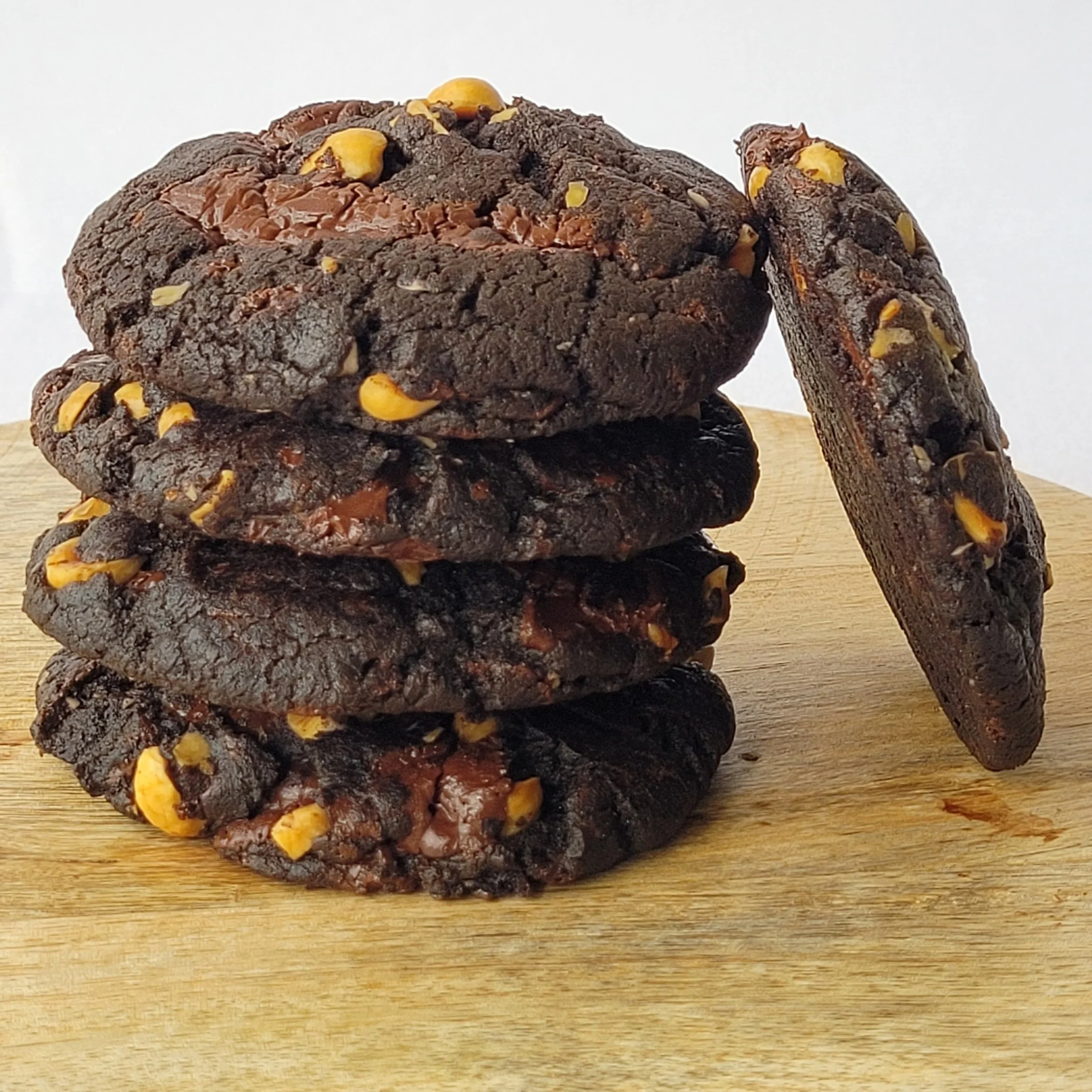 Stack of five chocolate cookies with nuts on a wooden surface, with one cookie leaning against the stack.