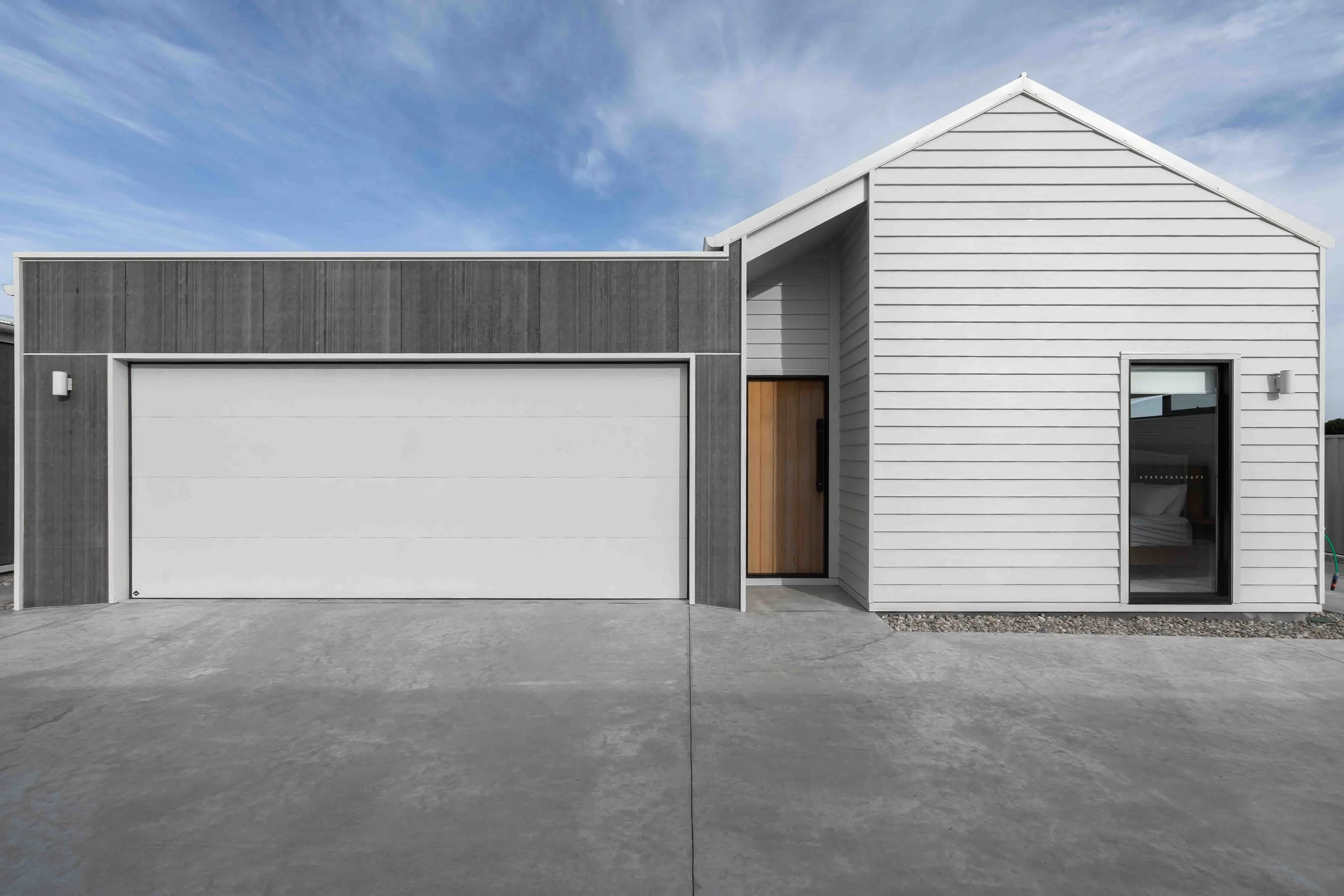 Exterior of modern beach side units with a wooden door and black frame, double car garage and pitched roof.