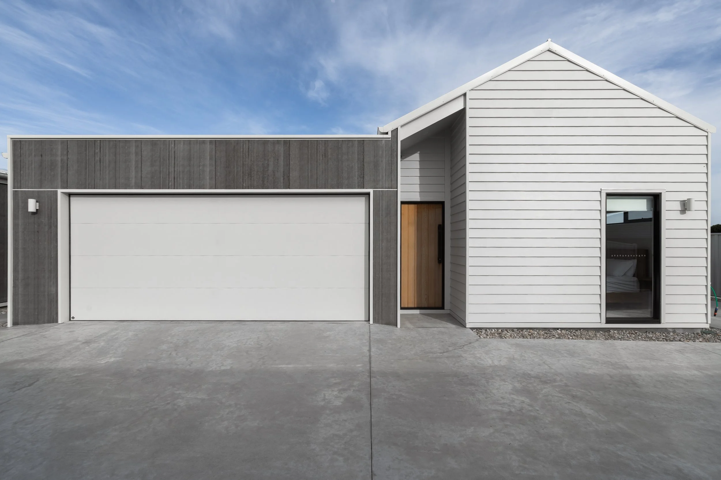 Entry way of Turners Beach units including dark grey garage and light grey house with light brown timber door.