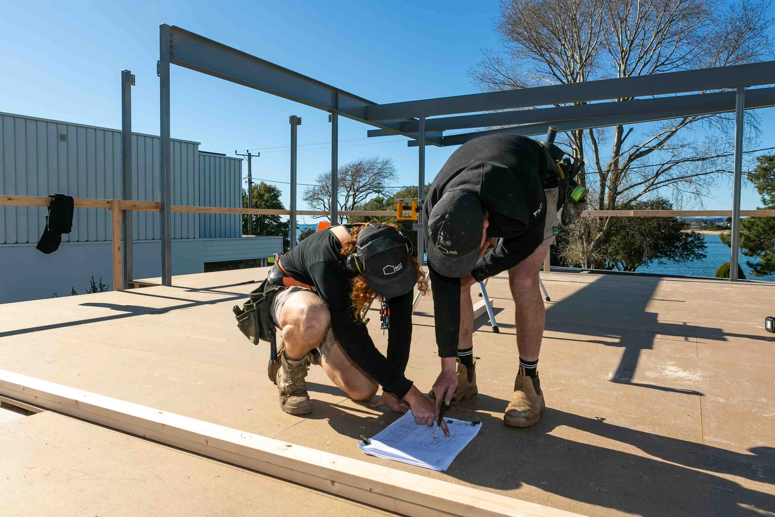 An image of two builders reviewing the plans of a house build on a bright sunny day.
