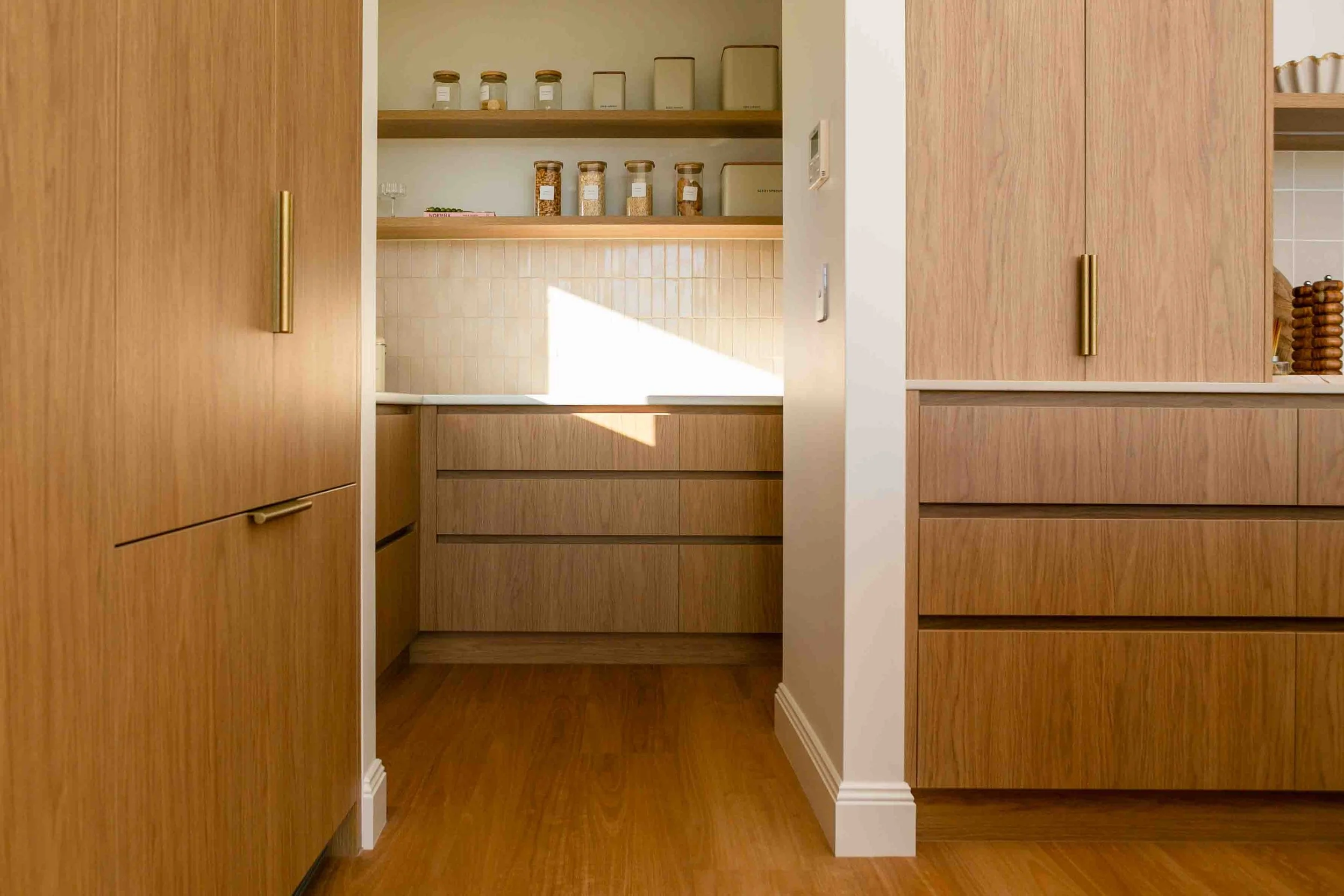A modern kitchen with timber cabinetry and gold metal handles and the entry to a spacious butler's pantry