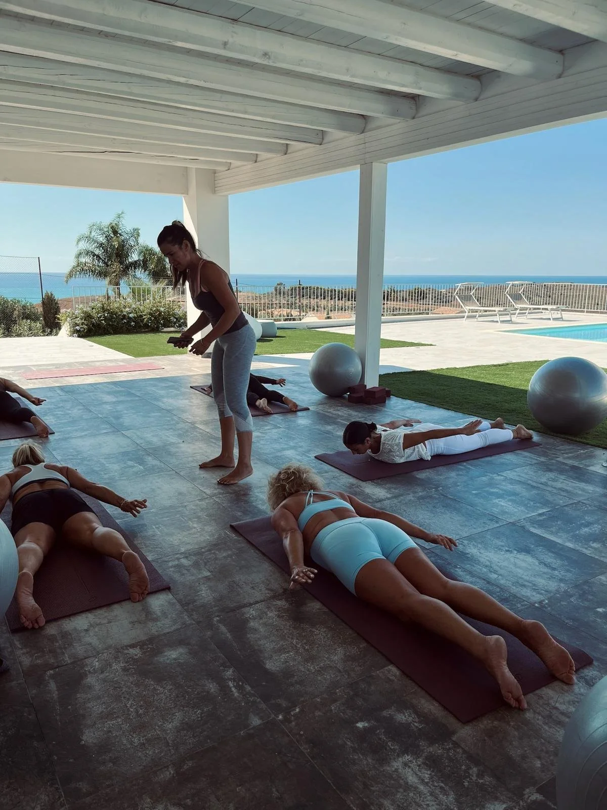 Groupe de personnes faisant du yoga sur un patio avec vue sur la mer, en plein jour.