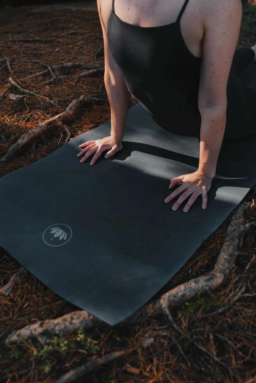 Nahaufnahme einer Frau, die beim Yoga in der Natur auf einem schwarzen Yoga-Matte kriecht, umgeben von Laub und Zweigen im Wald.