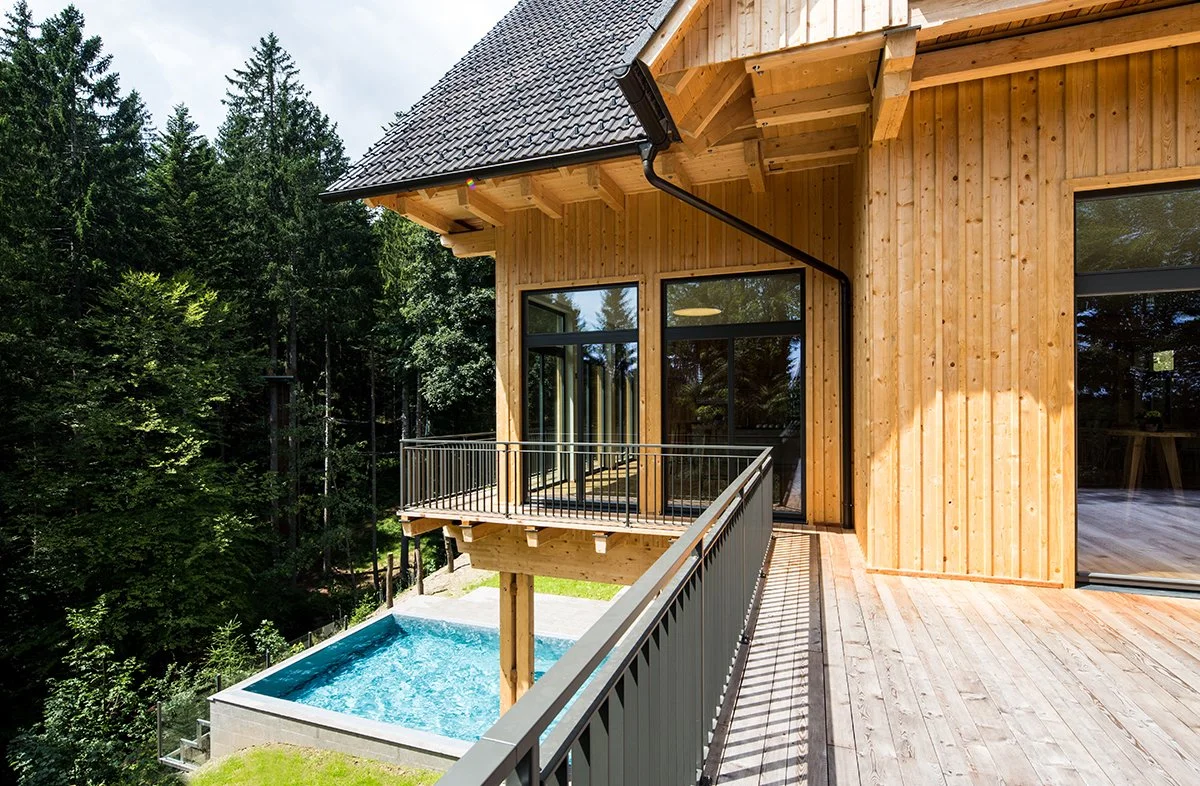 Holzhaus mit Balkon und Blick auf einen Pool, umgeben von Bäumen.