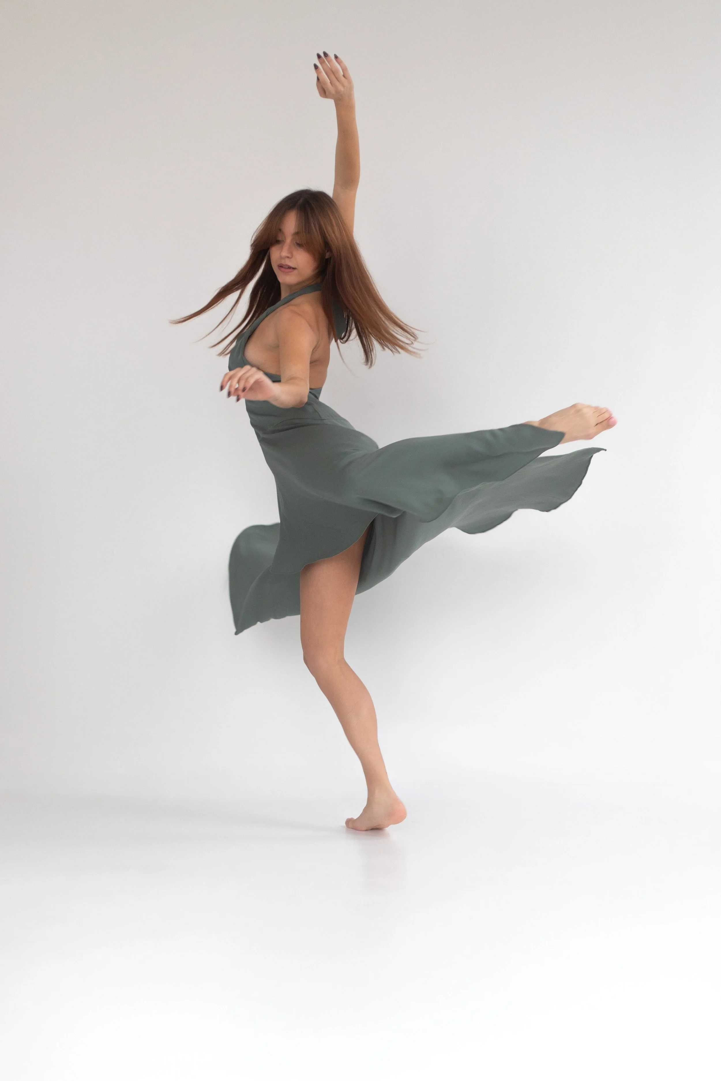 Une femme danse en équilibre avec une jambe levée et un bras en l'air dans un espace blanc minimaliste.