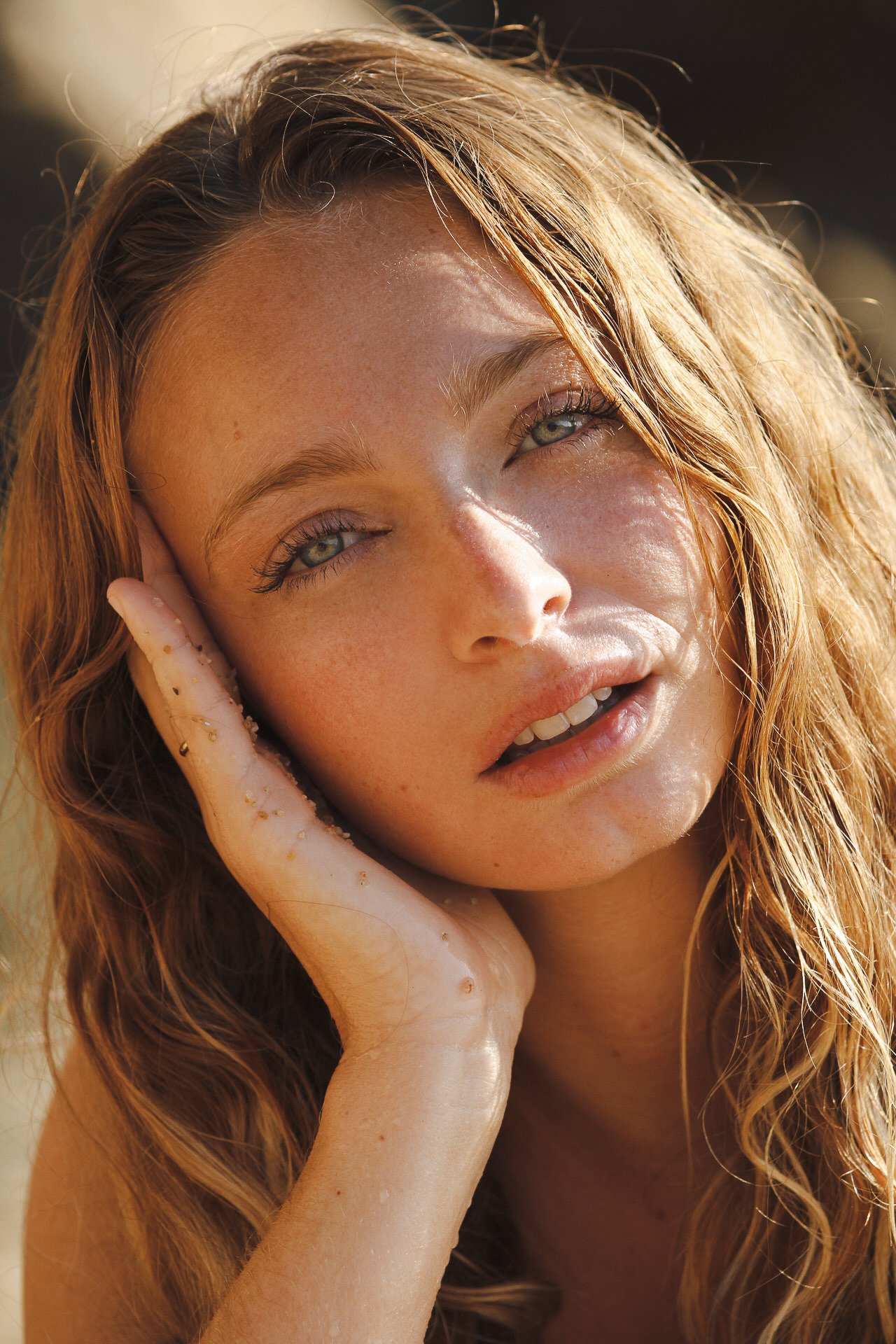 Portrait d'une jeune femme rousse avec des yeux clairs, posant avec la main contre la tête, éclairée par la lumière naturelle du soleil.