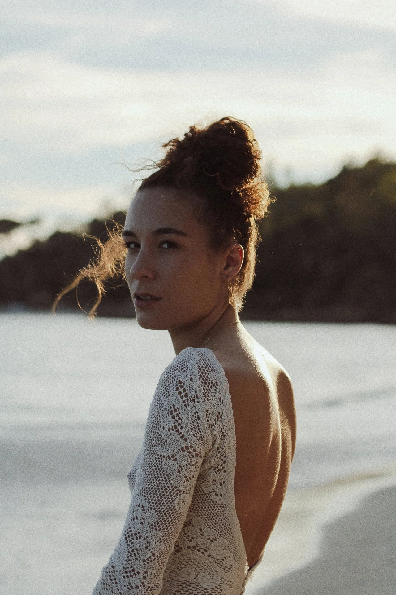 Une femme avec une coiffure en chignon sur la tête, portant une robe en crochet blanc, se tenant sur la plage