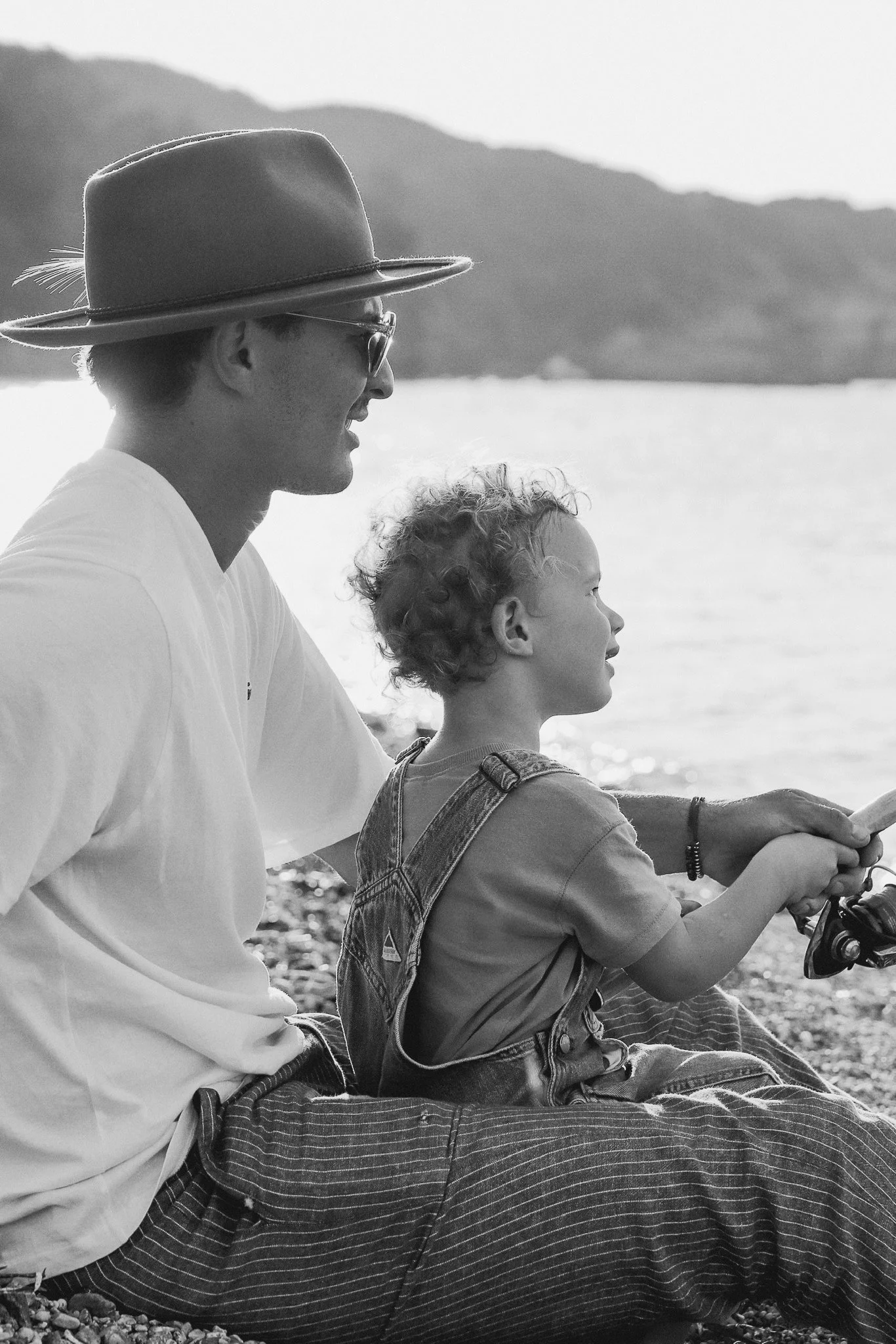 Un homme et un jeune garçon assis ensemble au bord d'un lac, pêchant, vues en noir et blanc.