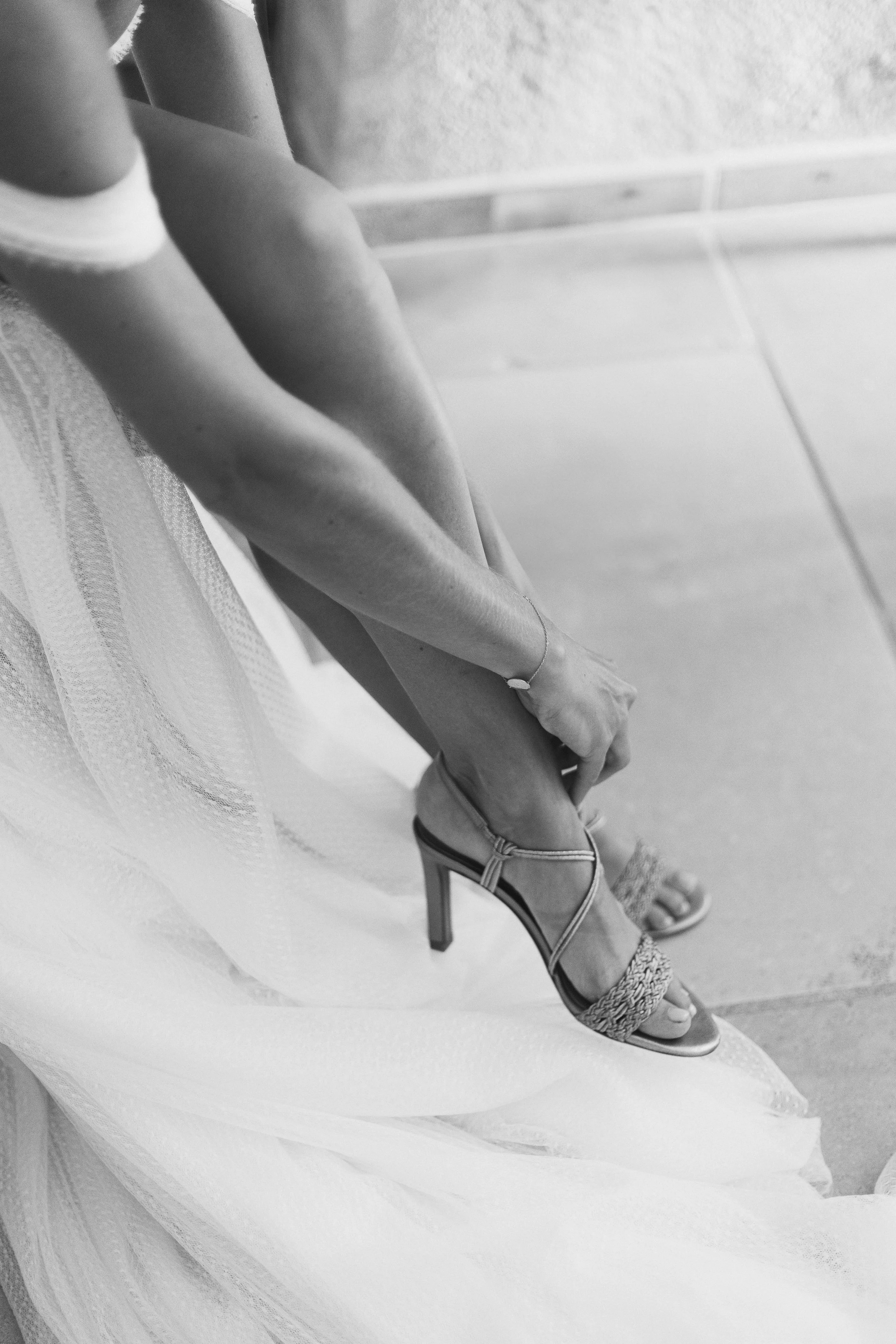 Une personne portant une robe de mariée et des sandales à talons ajustant sa cheville.