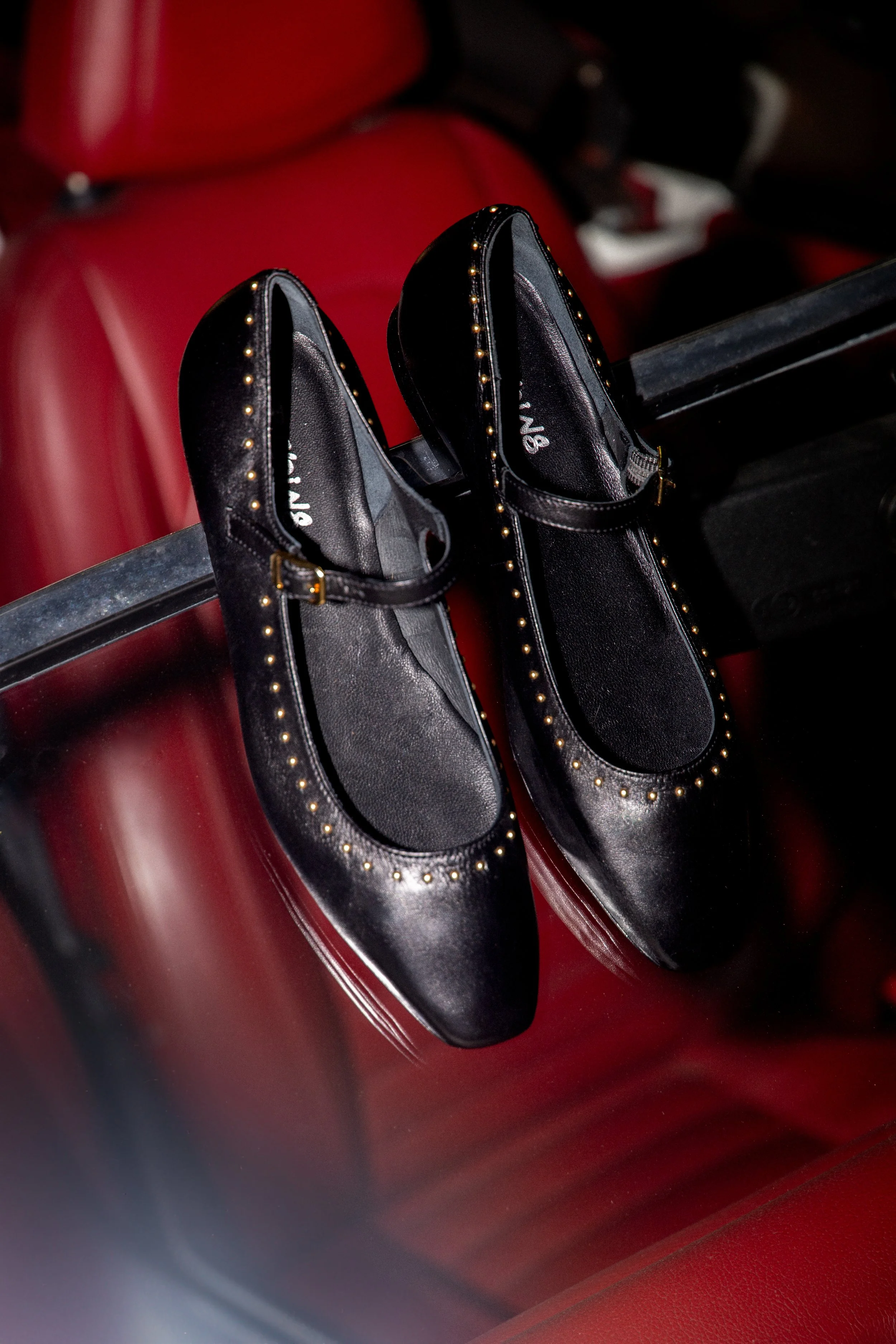 Une paire de chaussures noires avec des clous dorés, posées sur un siège en cuir rouge.