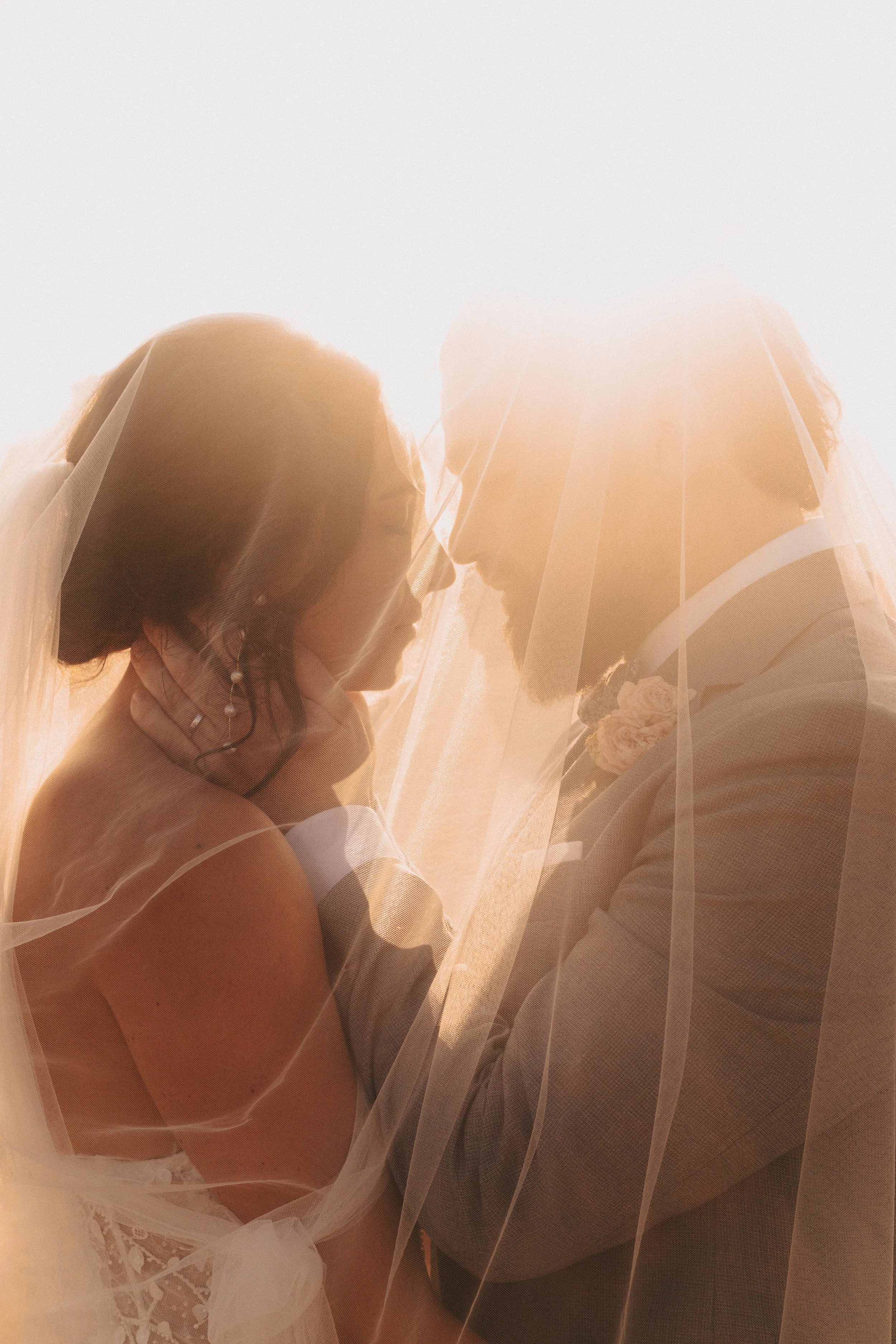 Un couple de mariés se regarde tendrement sous un voile de mariée, lors d'une séance photo de mariage.