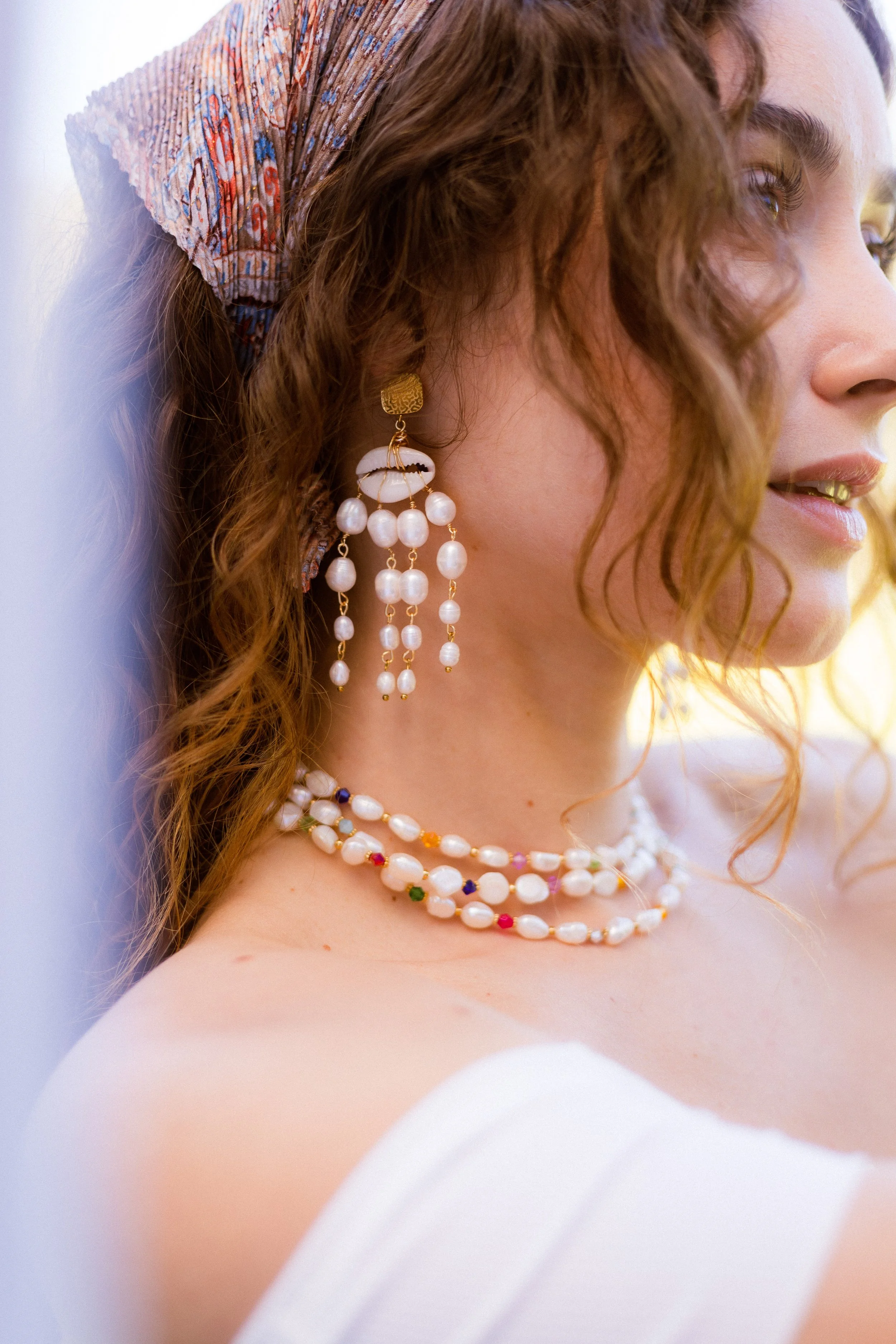 Une femme porte des boucles d'oreilles longues et une chaîne en perles, avec un foulard coloré dans ses cheveux.