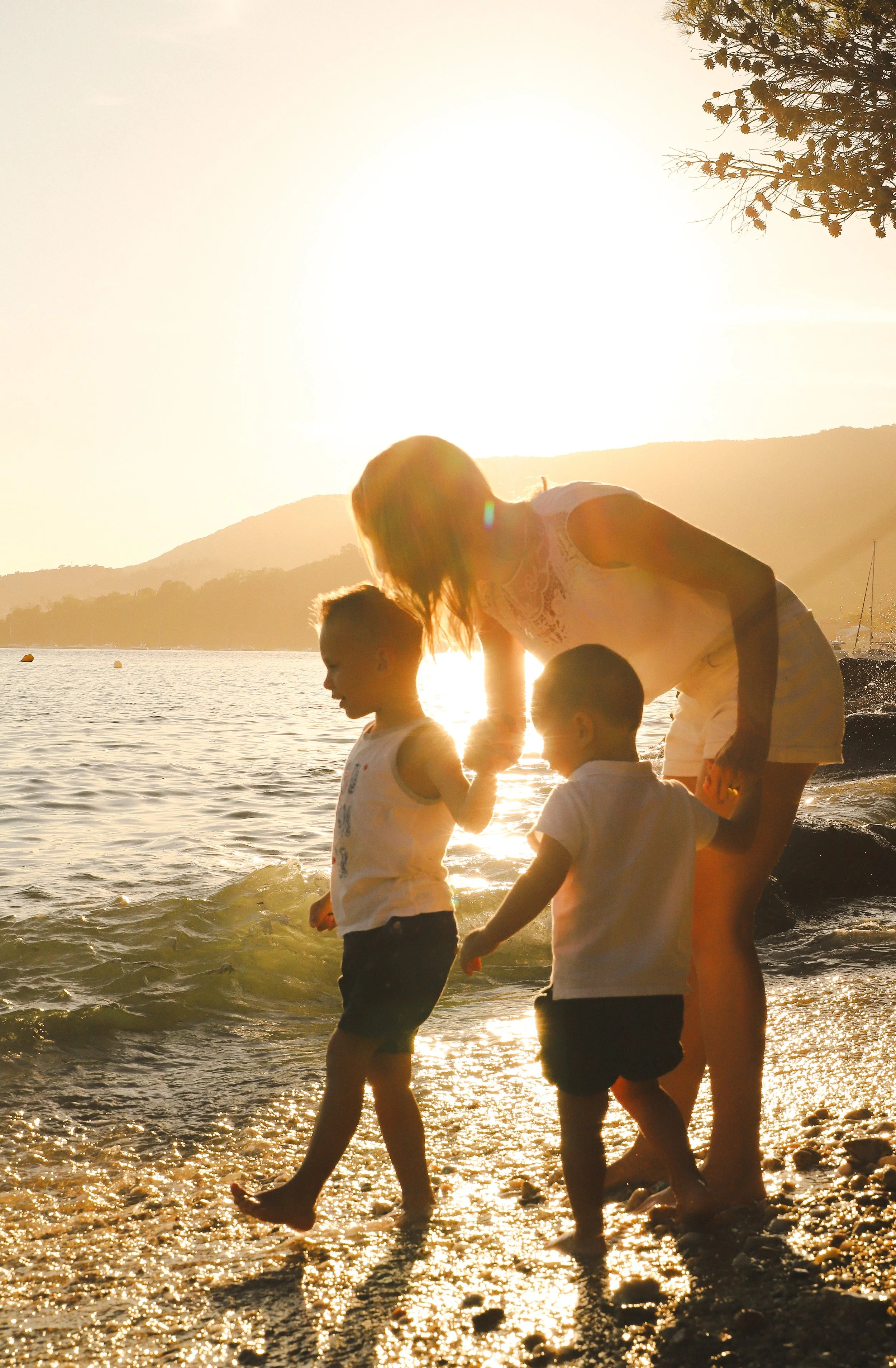Une mère avec ses deux enfants jouent au bord de la mer au coucher du soleil.
