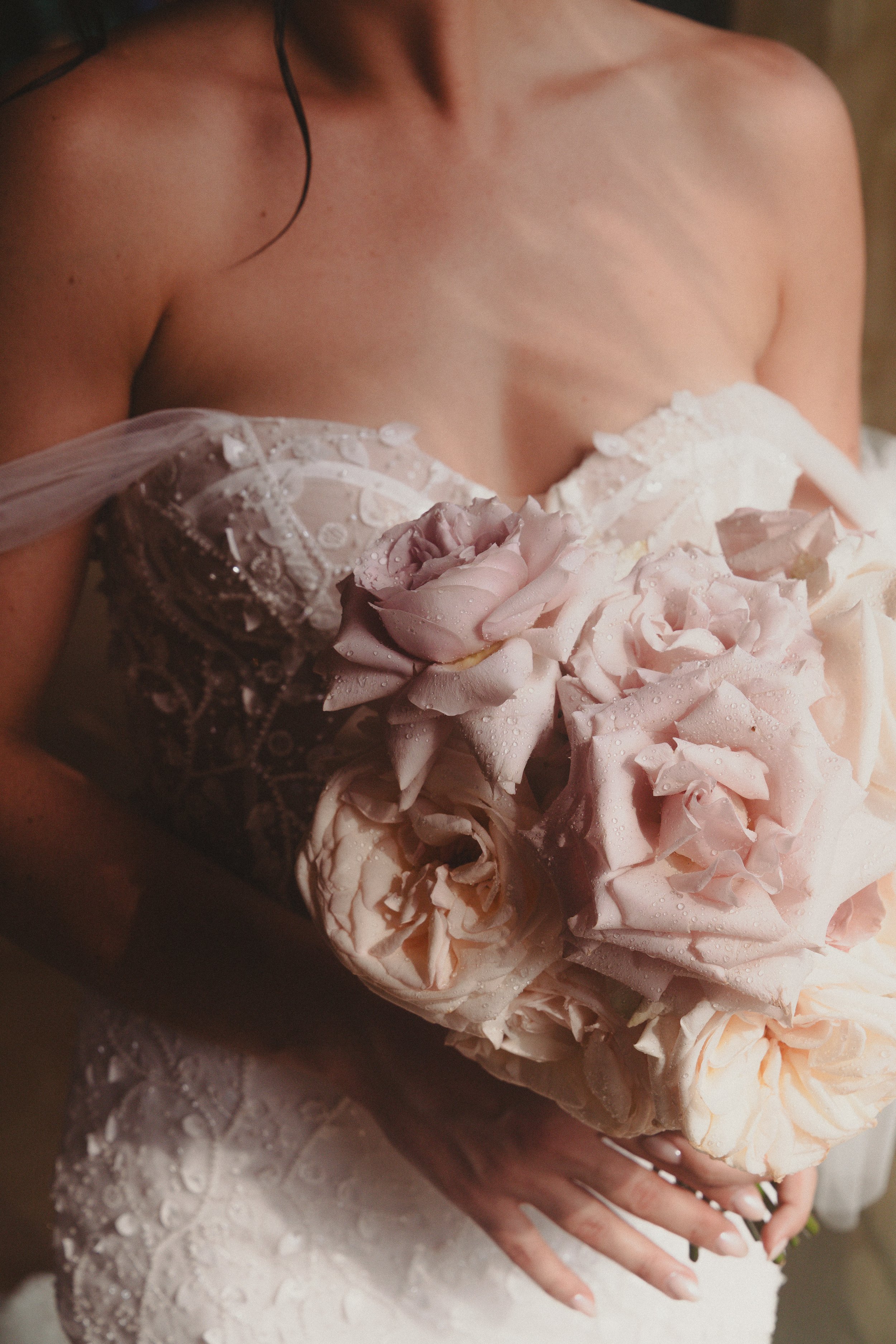 Femme en robe de mariage tenant un bouquet de roses pale, avec des gouttes d'eau sur les fleurs.