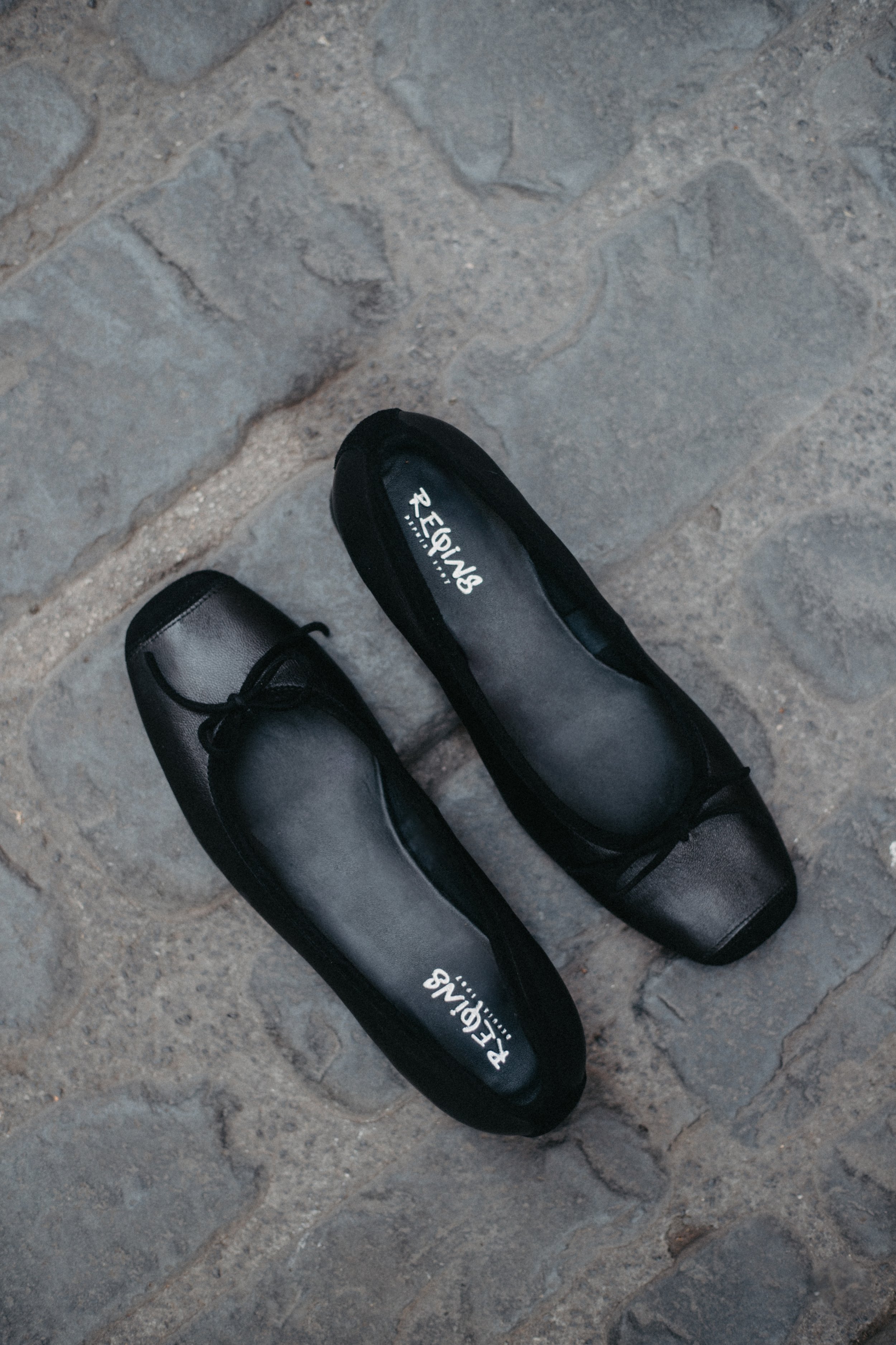 Une paire de chaussures noires en cuir plate, posées sur un pavé de pierre.