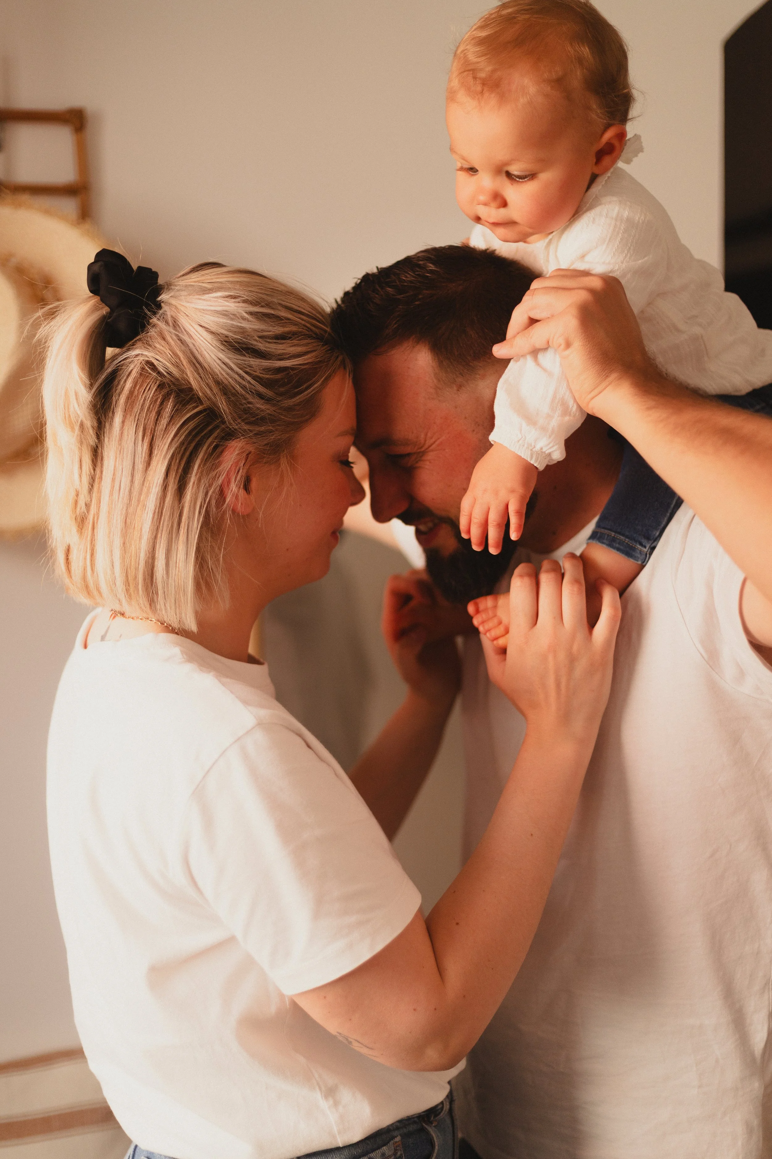 Une famille souriante se câline et joue ensemble, formée d'une femme, d'un homme et d'un bébé.