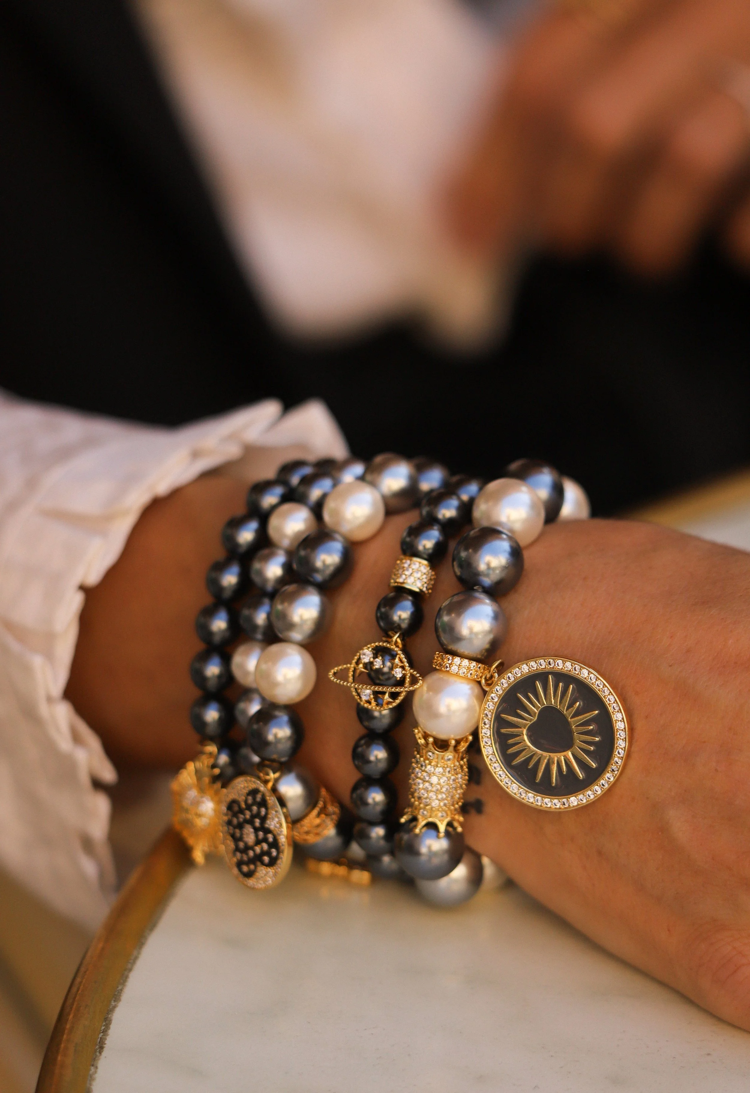 Poignée de bracelets en perles noires et blanches avec des pendentifs en or et imitation de pierres précieuses, certains ornés de petites pierres brillantes.