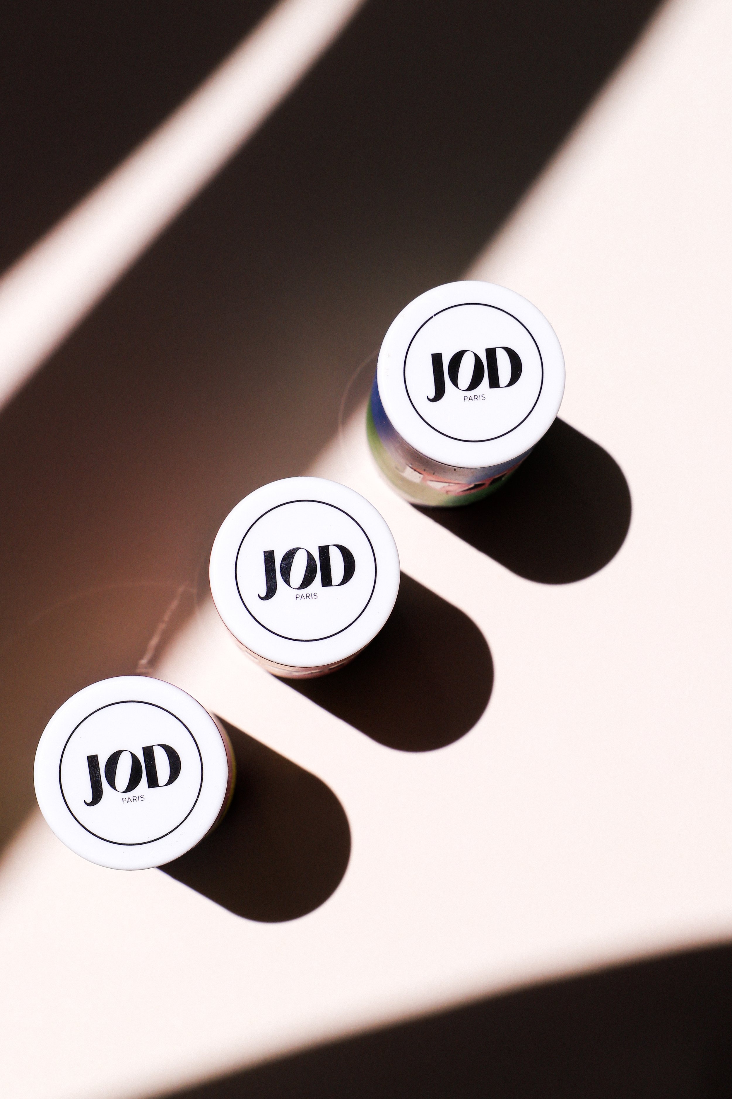 Trois petits pots de crème glacée de la marque JOD Paris, posés sur une surface claire, avec des ombres noires distinctes dûes à la lumière.