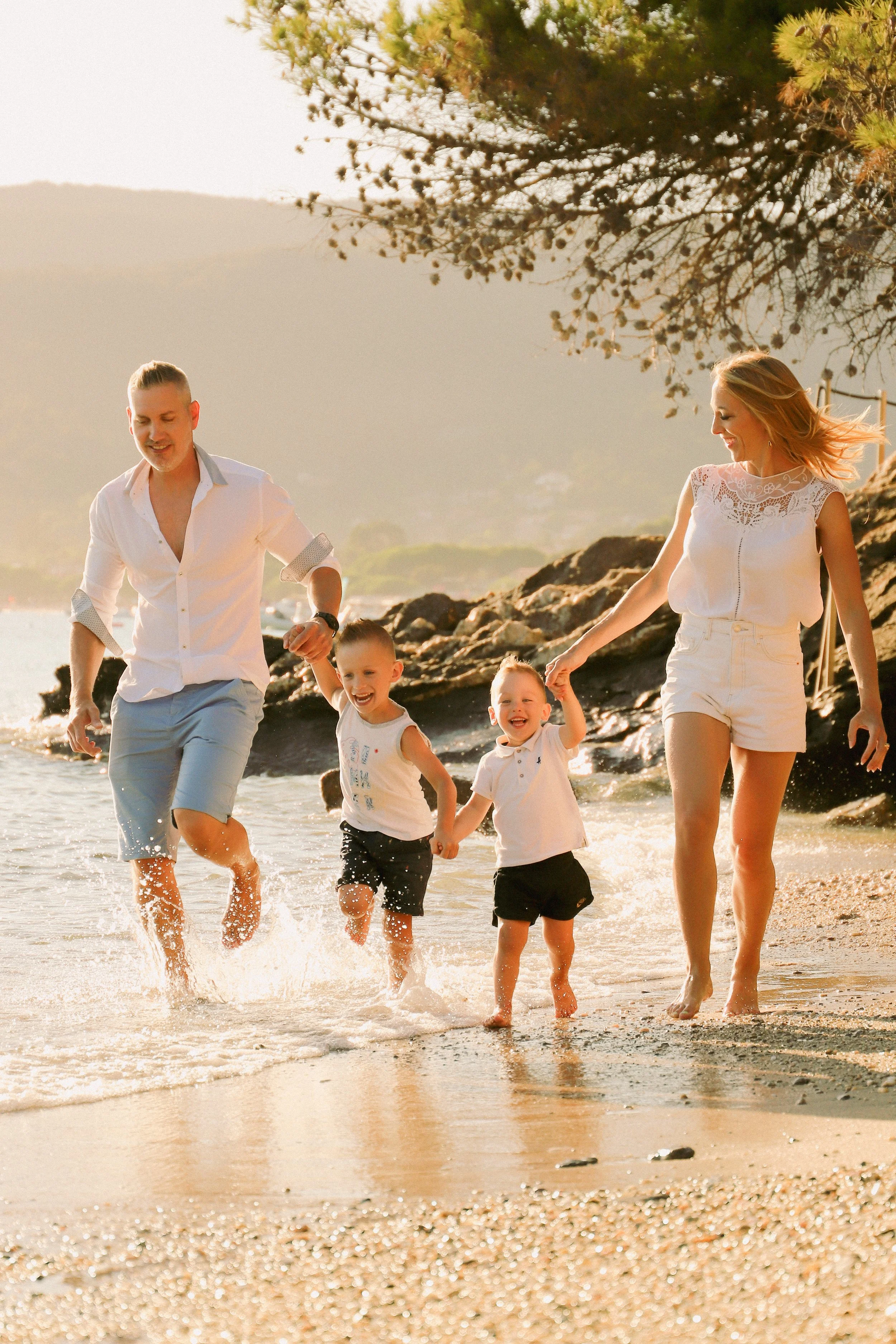 Une famille heureuse, comprenant deux adultes et deux jeunes enfants, qui joue et court dans l'eau à la plage lors du coucher du soleil.