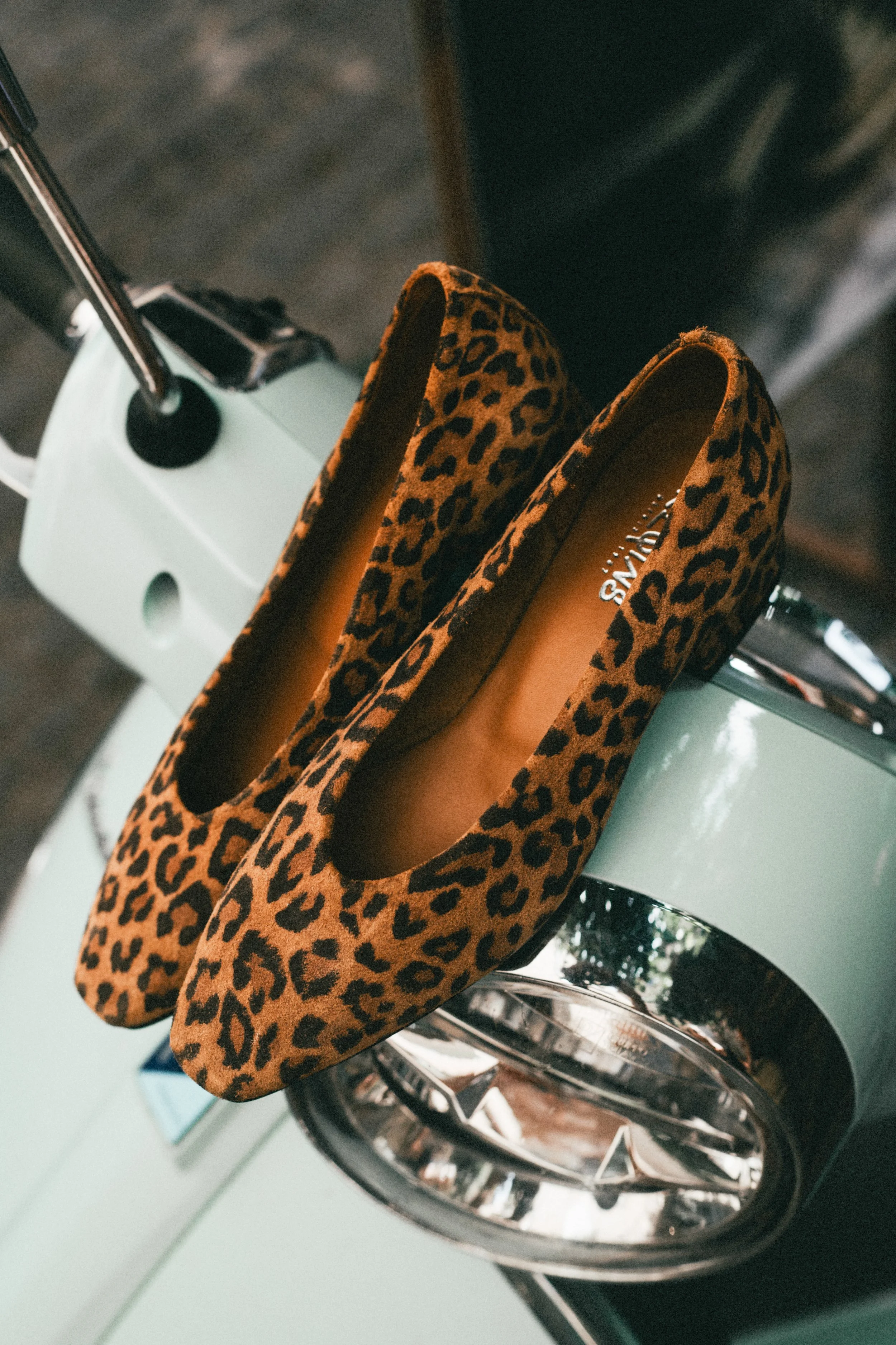 Une paire de chaussures à imprimé léopard posée sur le porte-bagages d'une petite voiture verte.