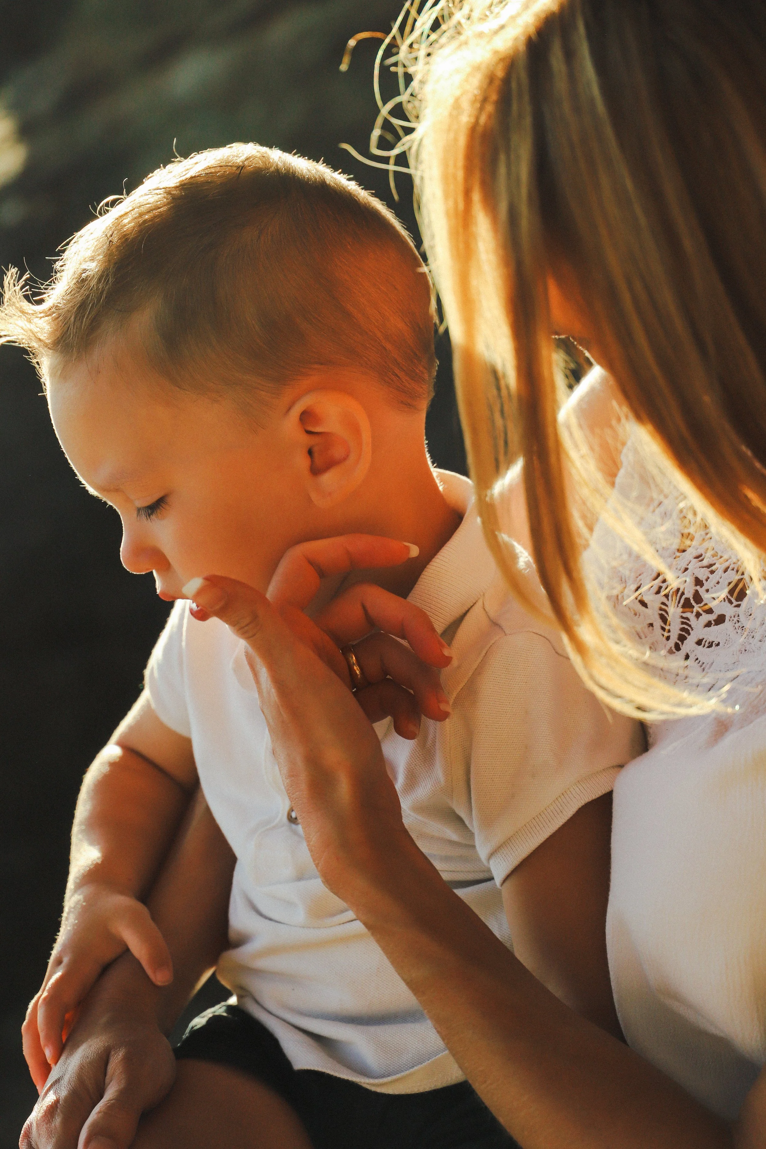 Une femme tient un jeune garçon dans ses bras, il a les yeux fermés et l'air pensif, dans une ambiance chaleureuse en lumière naturelle.