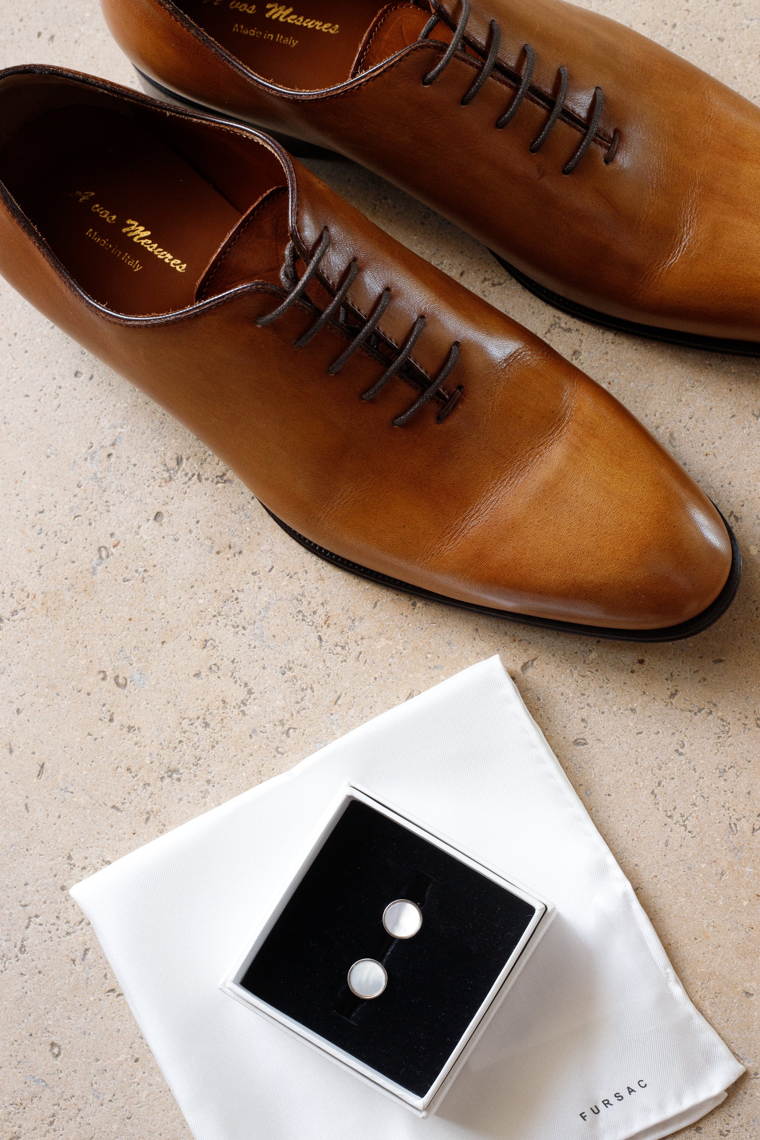 Une paire de chaussures en cuir marron, une boîte à boutons et un tissu blanc sur une surface en pierre.