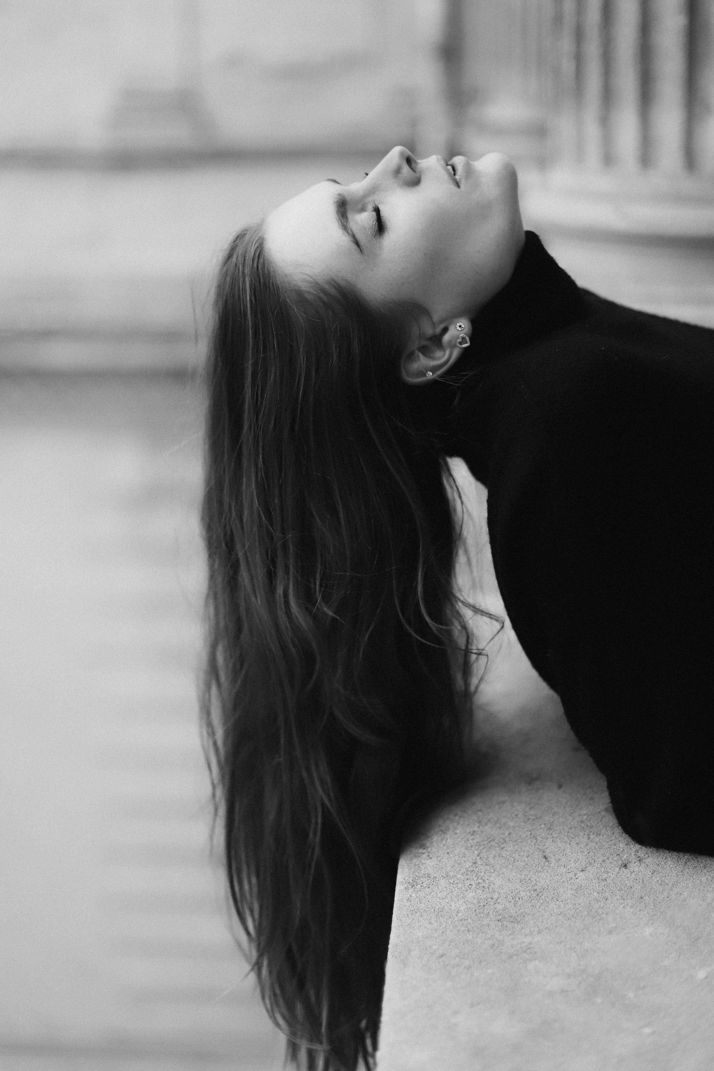Une femme aux cheveux longs, portant un pull noir, est allongée sur le sol avec la tête inclinée en arrière et les yeux fermés, en noir et blanc.