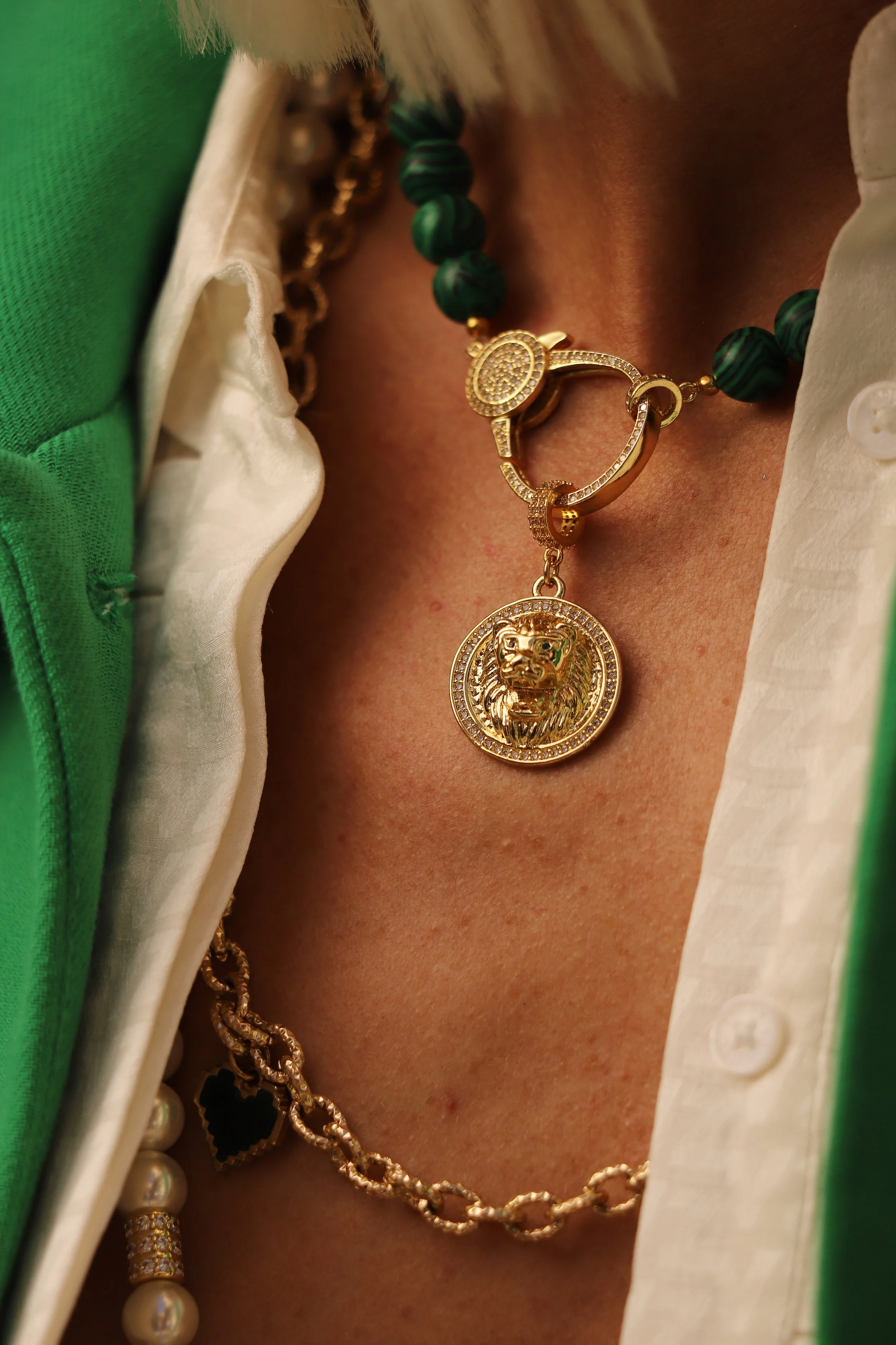 Close-up de colliers en or, dont un avec un pendentif de tête de lion, porté avec des vêtements colorés.