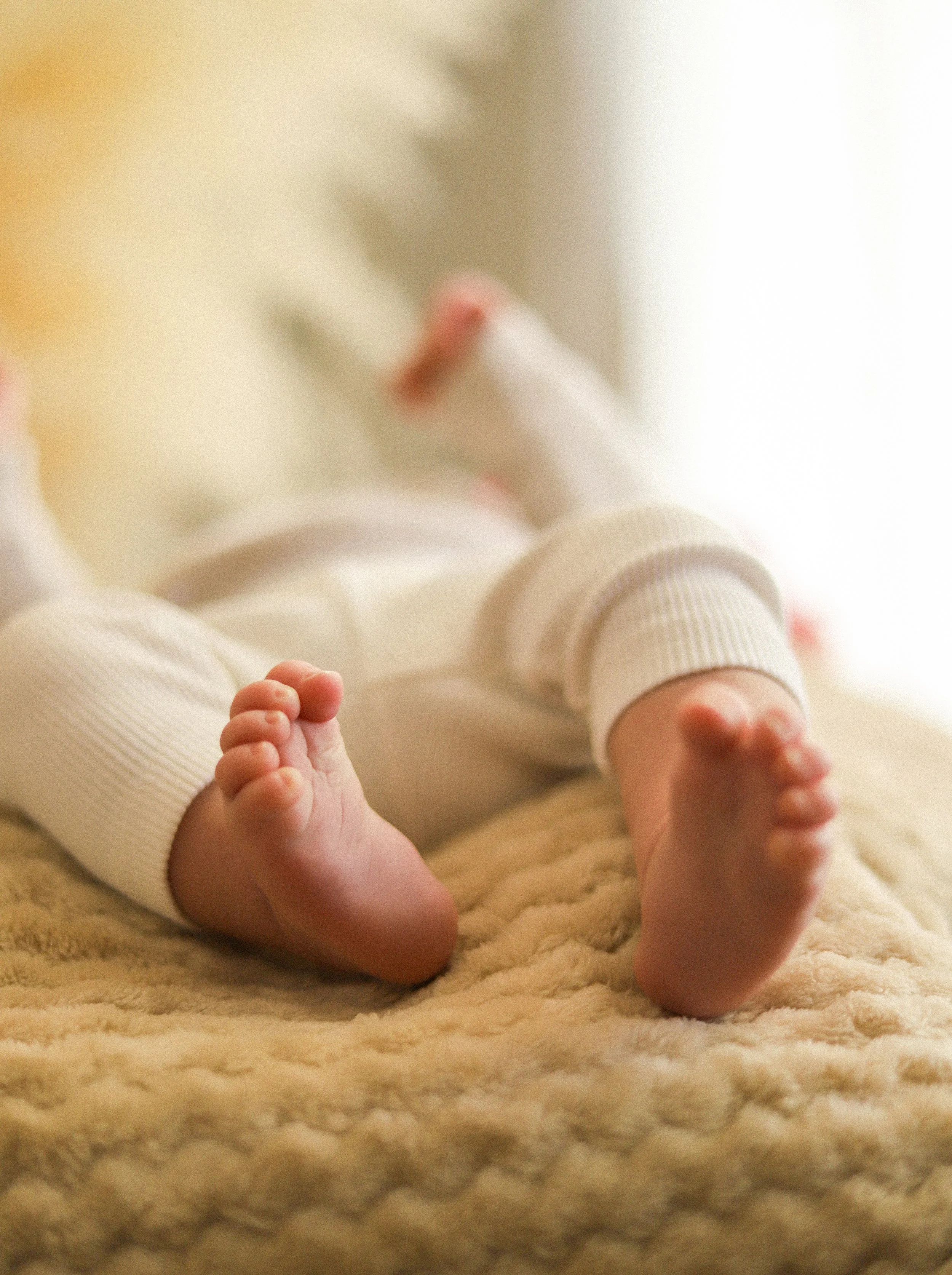 Les pieds d'un bébé allongé sur une couverture douce, vêtu d'un sweat blanc et de pantalons en coton blanc.