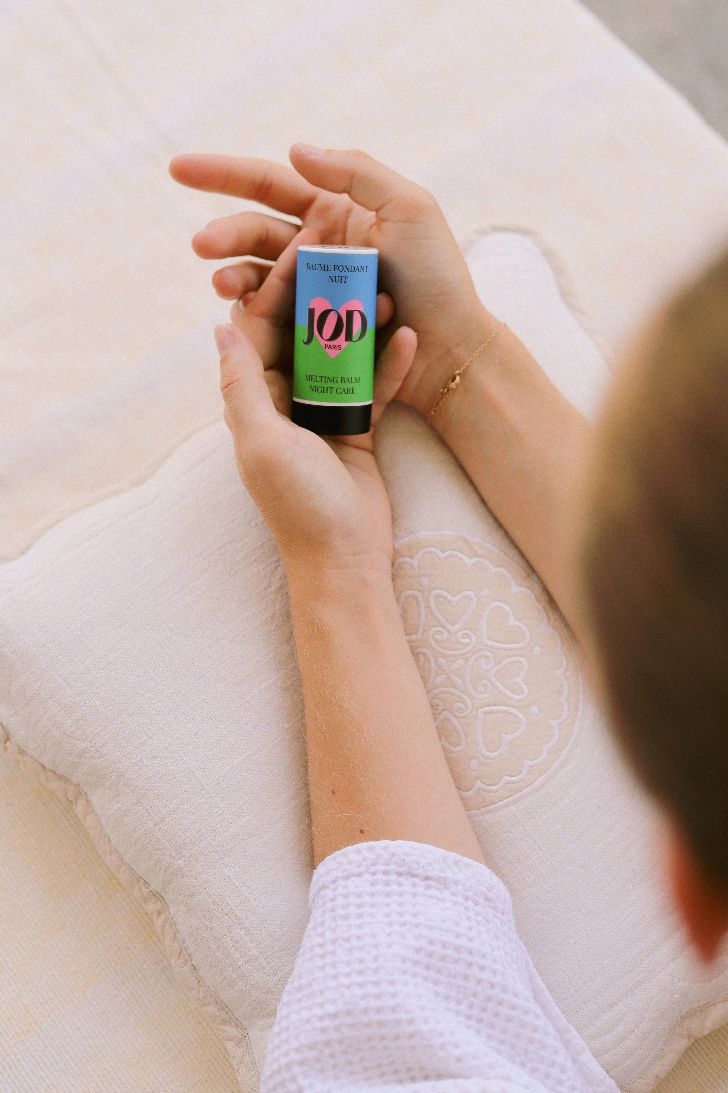 Une personne allongée sur un canapé blanc, tenant un baume fondant Nuit JOD dans la main.