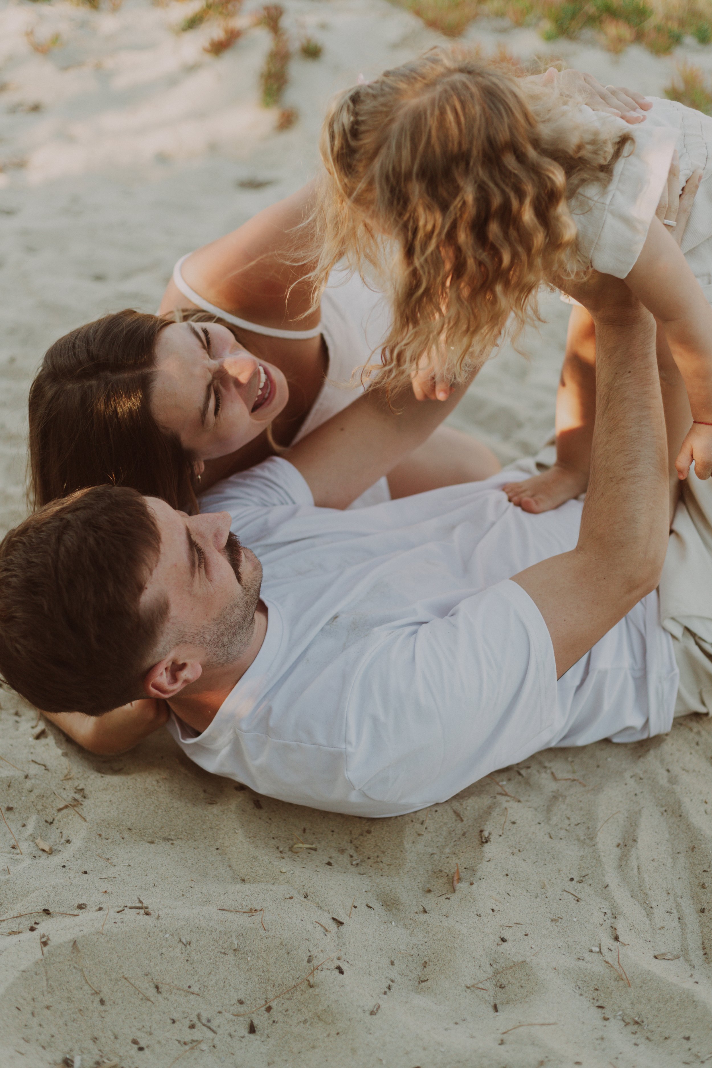 Une famille joue et s'amuse sur la plage, un père, une mère et une fille se tenant en souriant et riant.