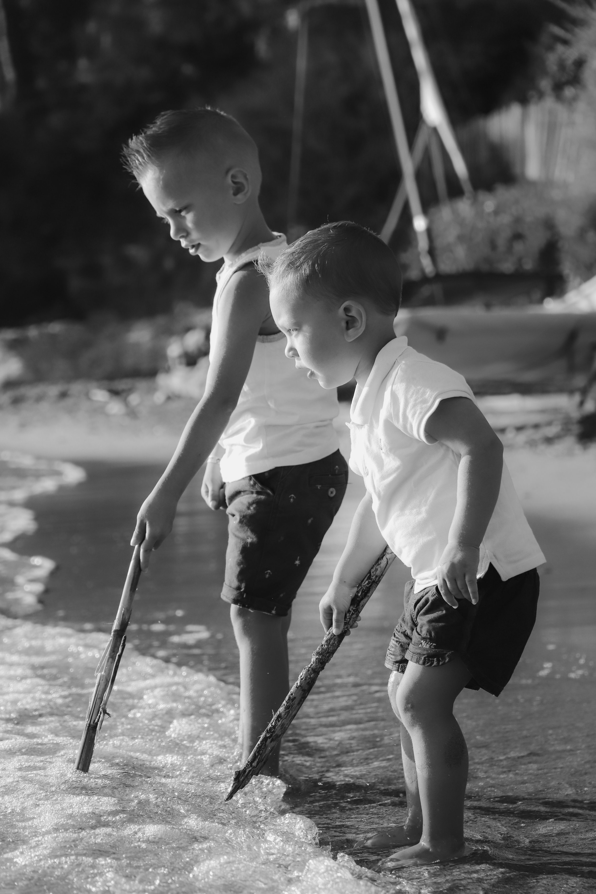 Deux jeunes garçons jouent avec des bâtons dans l'eau à la plage.