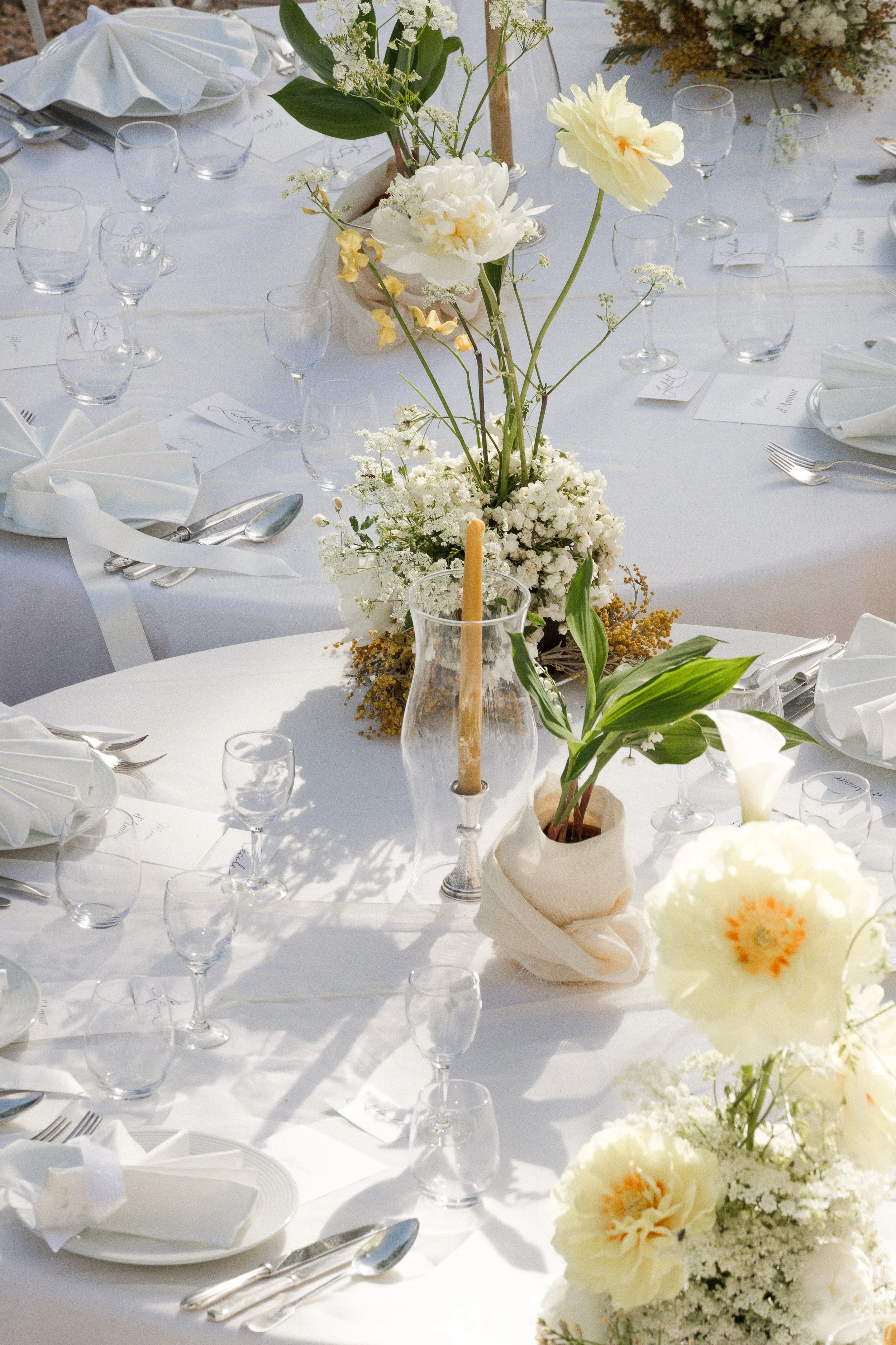 Une table élégante décorée avec des fleurs blanches et crème, des verres à vin, des assiettes, des couverts, des bougies et des papiers de menu, prête pour un événement formel.