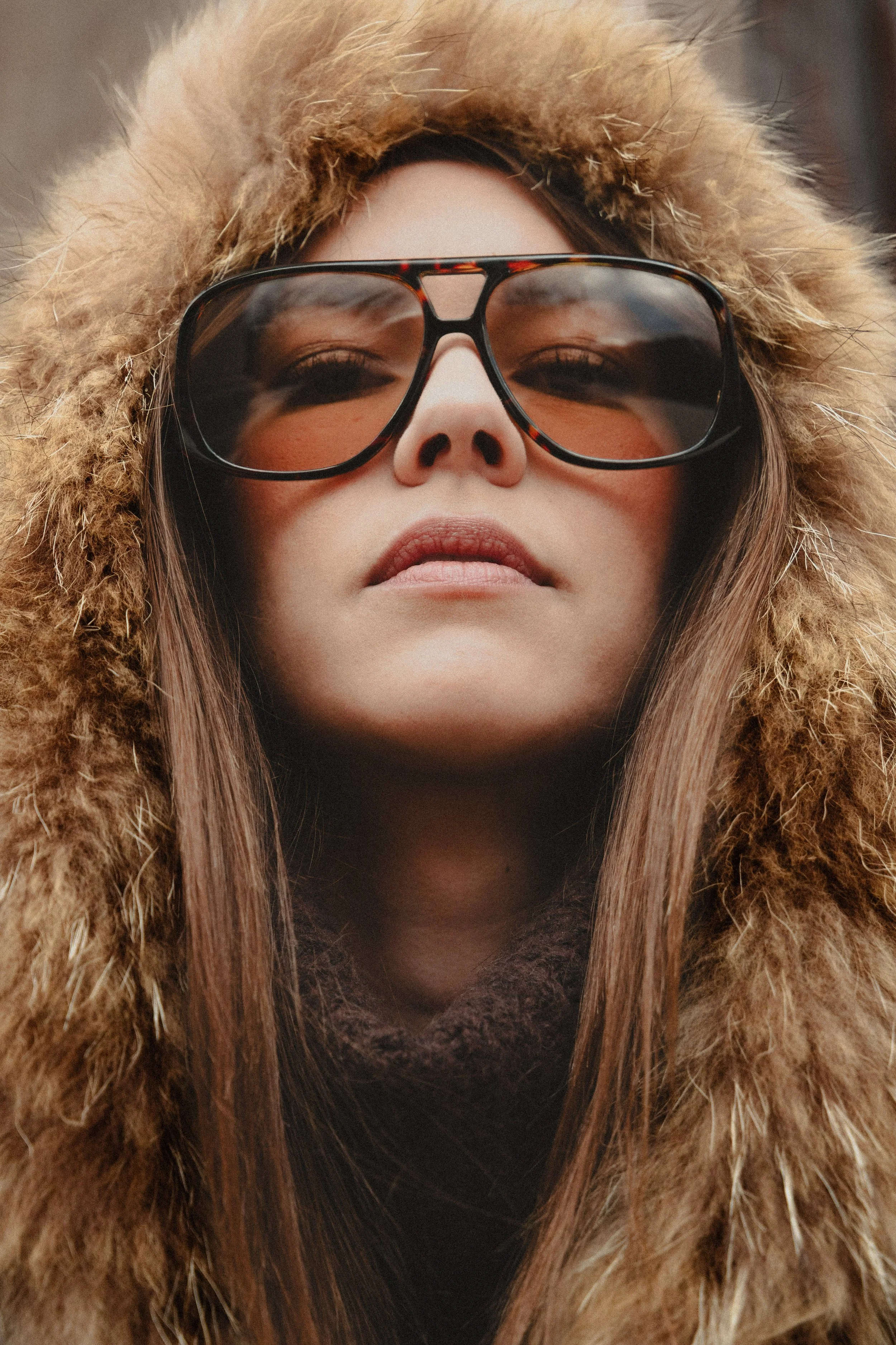 Vue en contre-plongée d'une femme portant des lunettes de soleil et un manteau en fourrure avec une capuche en fourrure.